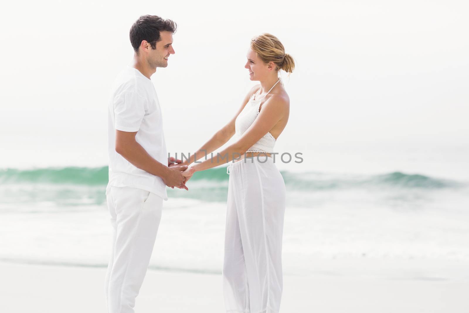 Romantic couple looking at each other and holding hands on the beach