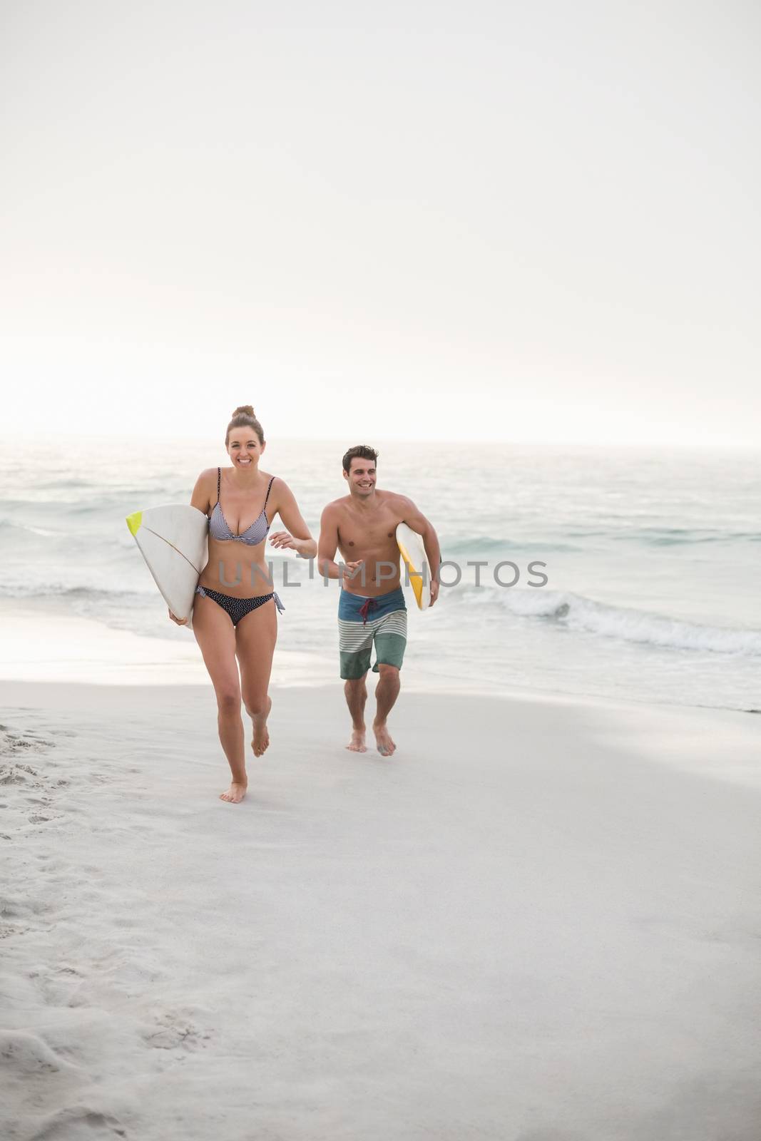 Couple with surfboard running on the beach on a sunny day