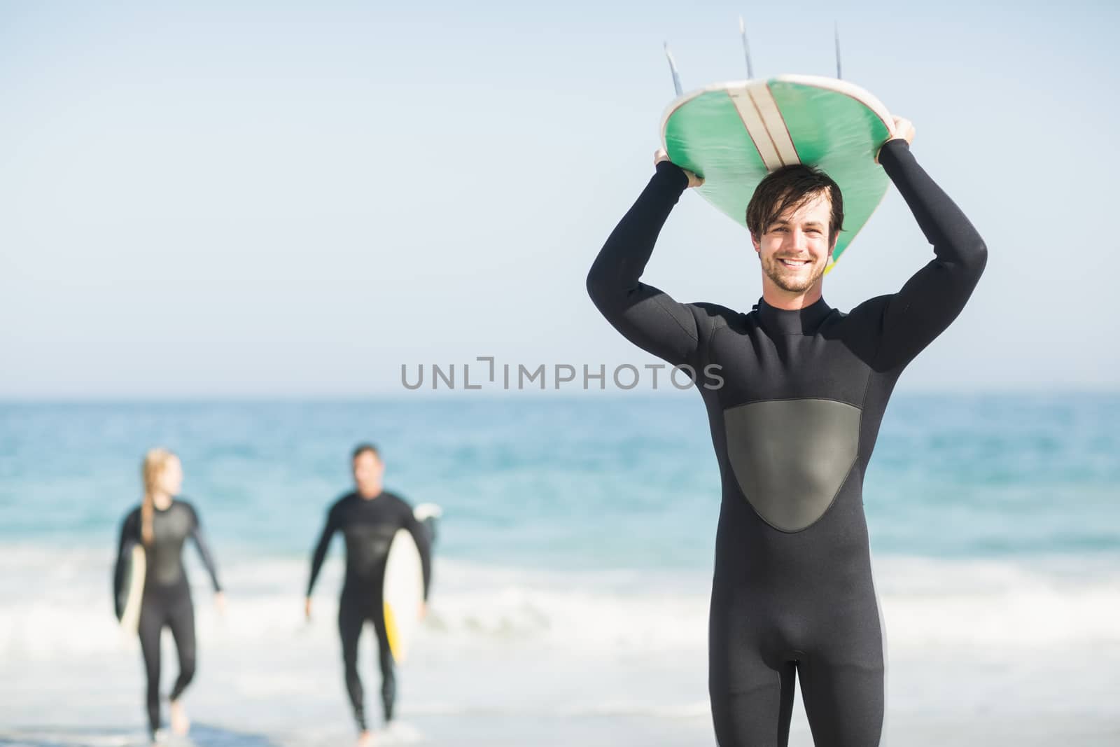 Happy man in wetsuit carrying surfboard over head by Wavebreakmedia