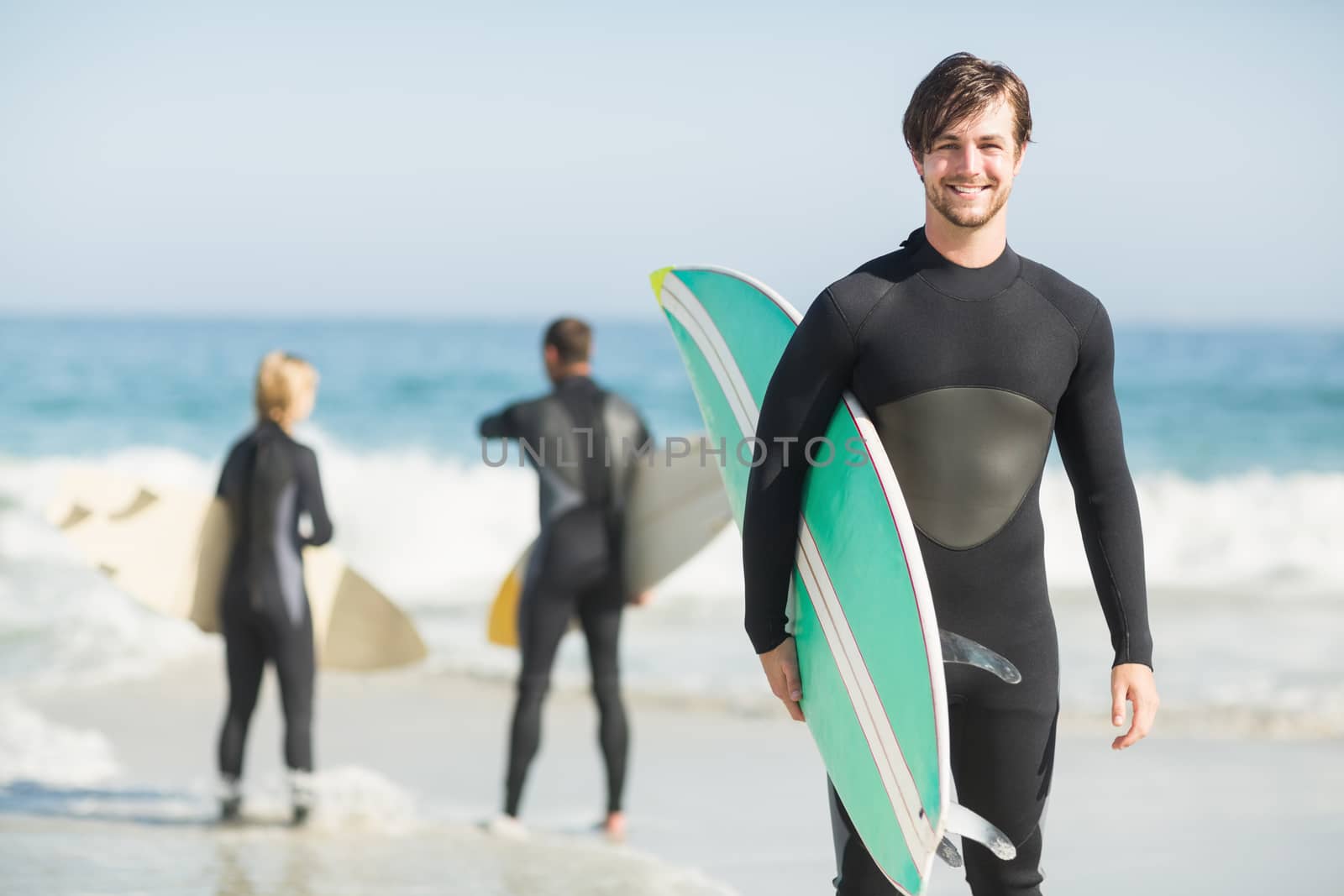 Portrait of happy man holding a surfboard on the beach by Wavebreakmedia