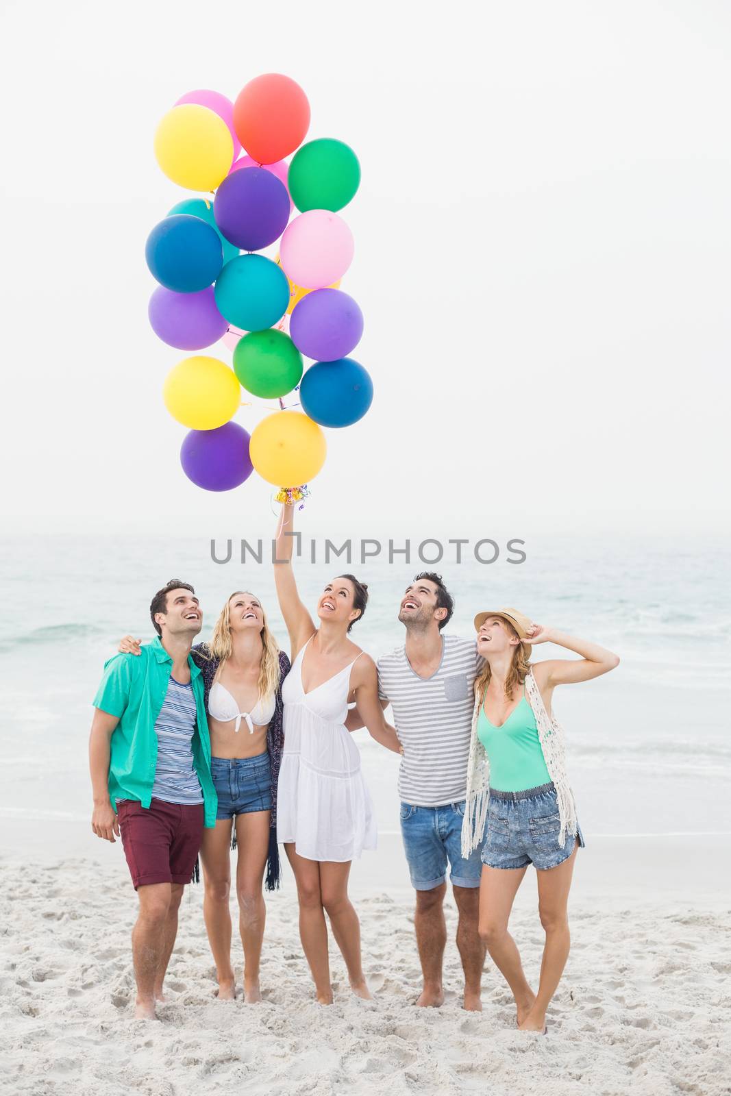 Group of happy friends standing on the beach with multicolored balloons