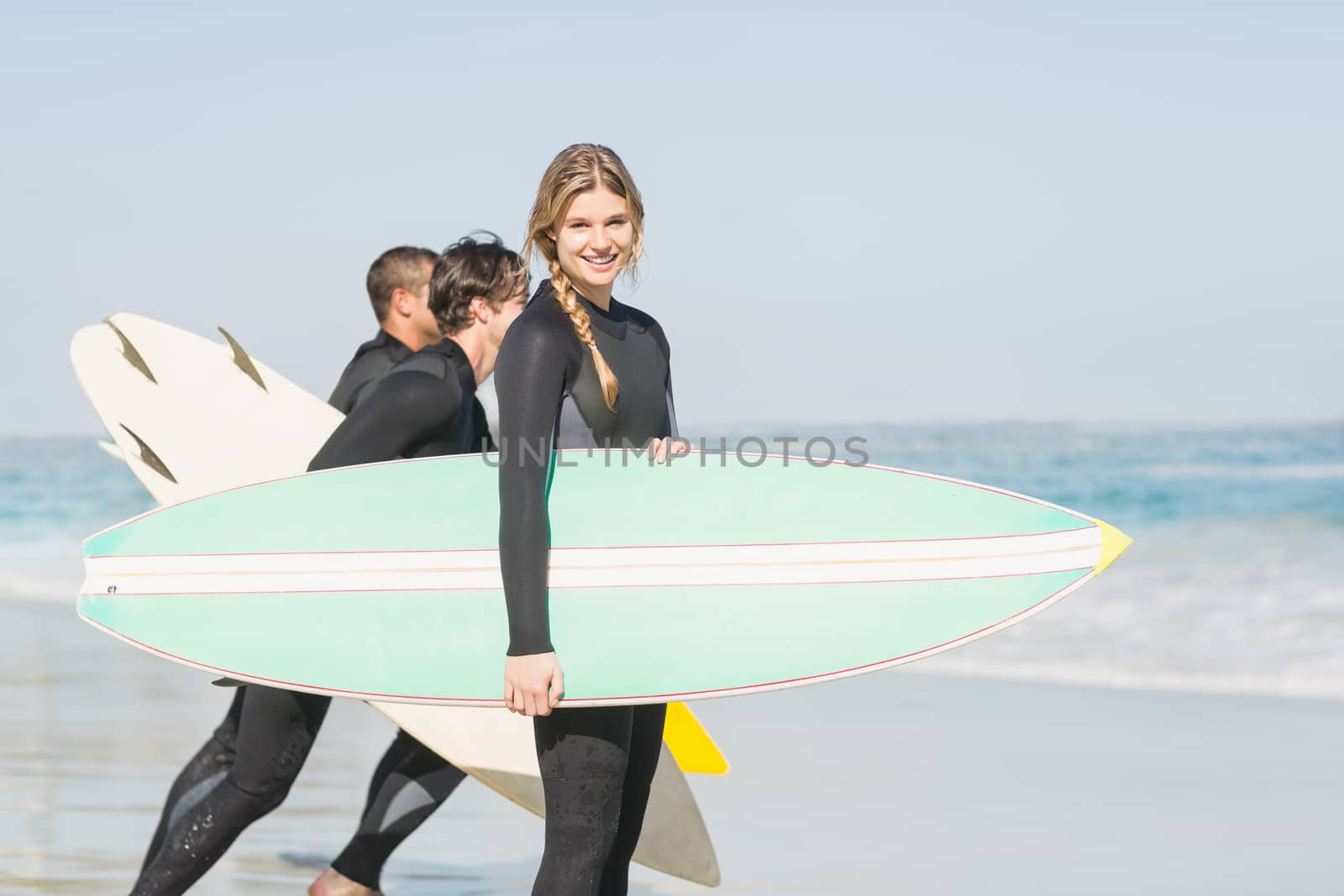 Portrait of surfer woman with surfboard standing on the beach and others surfer in background