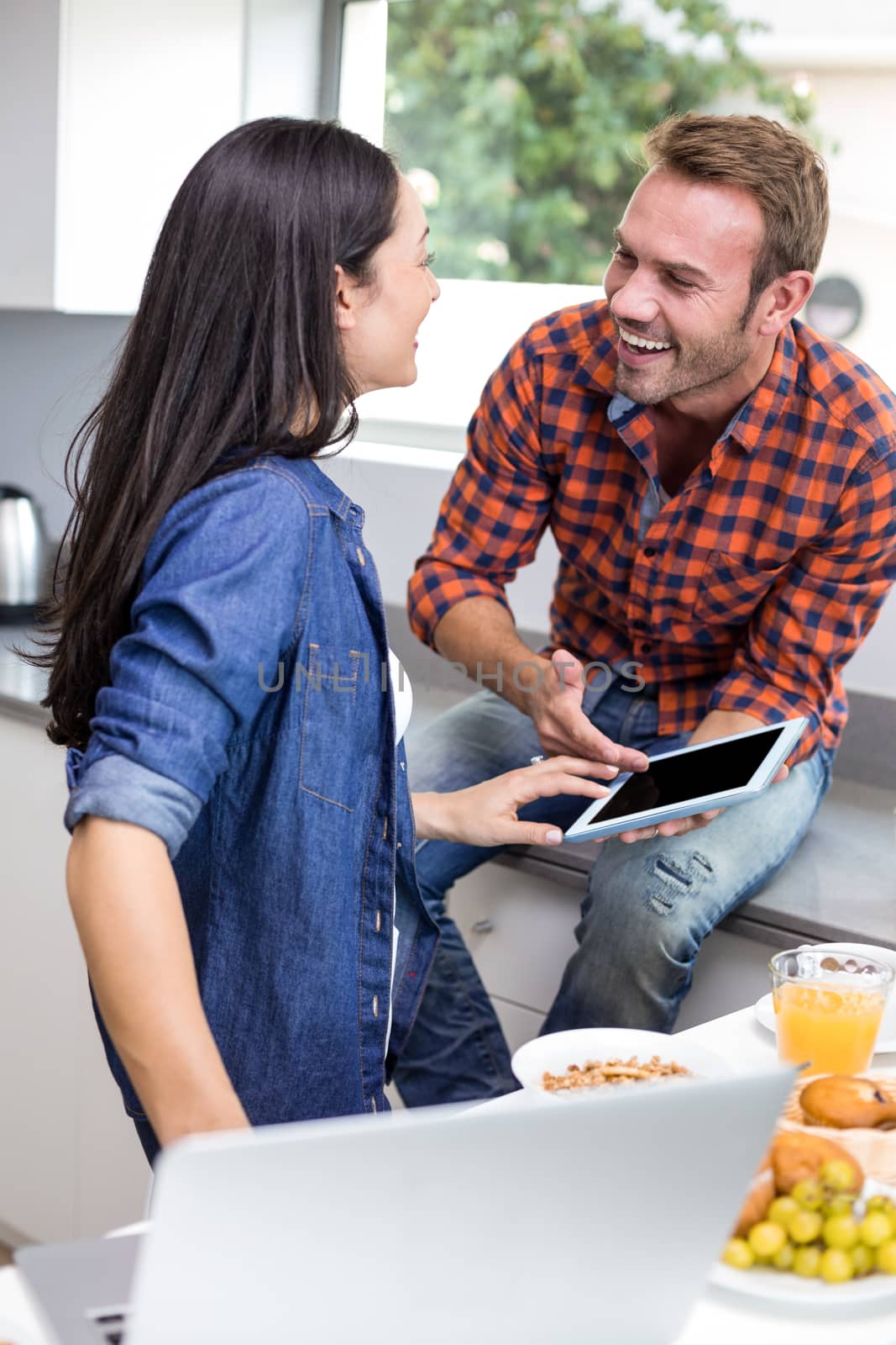 Couple interacting using laptop and digital tablet in the kitchen