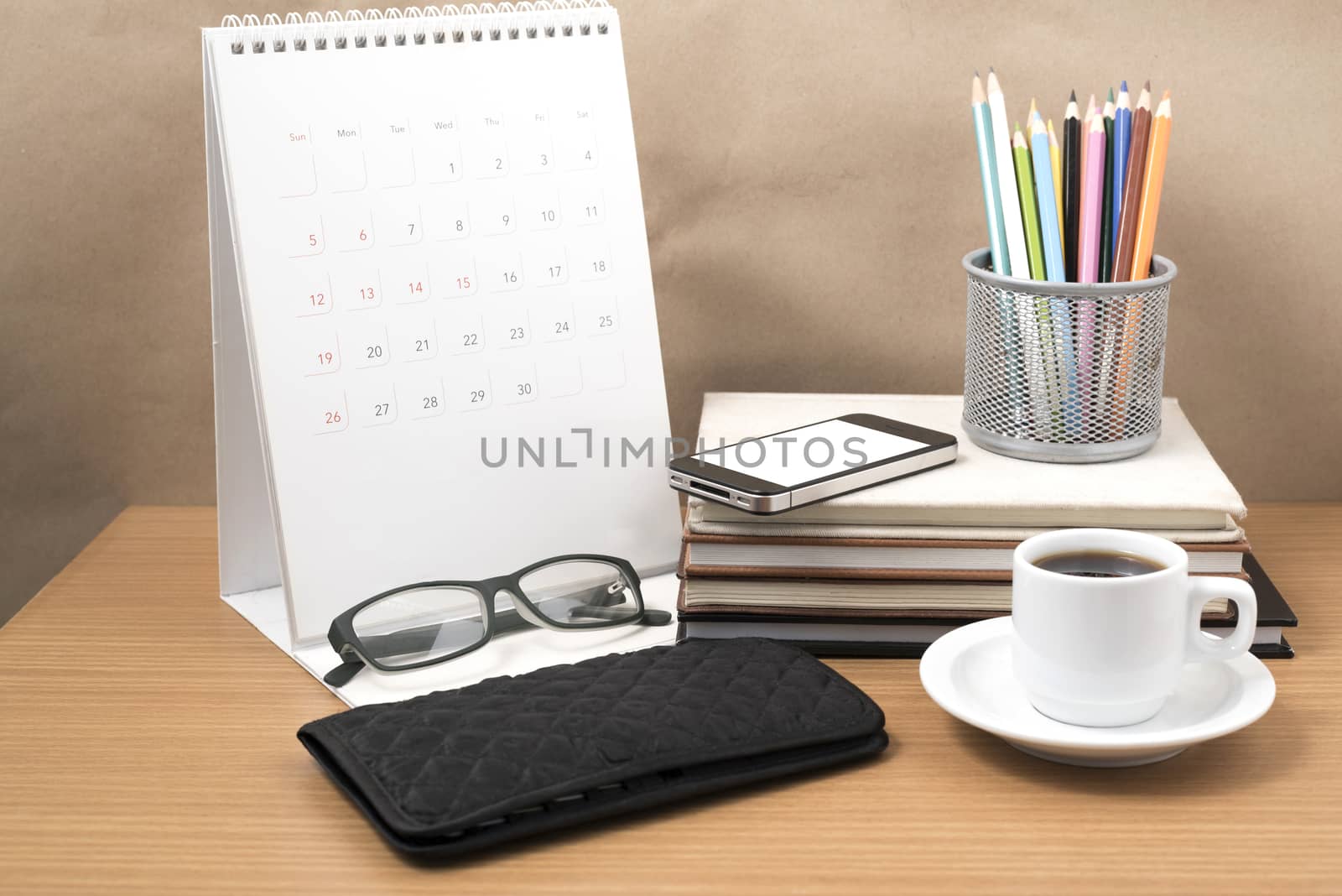 office desk : coffee with phone,wallet,calendar,color pencil box,stack of book,eyeglasses on wood background