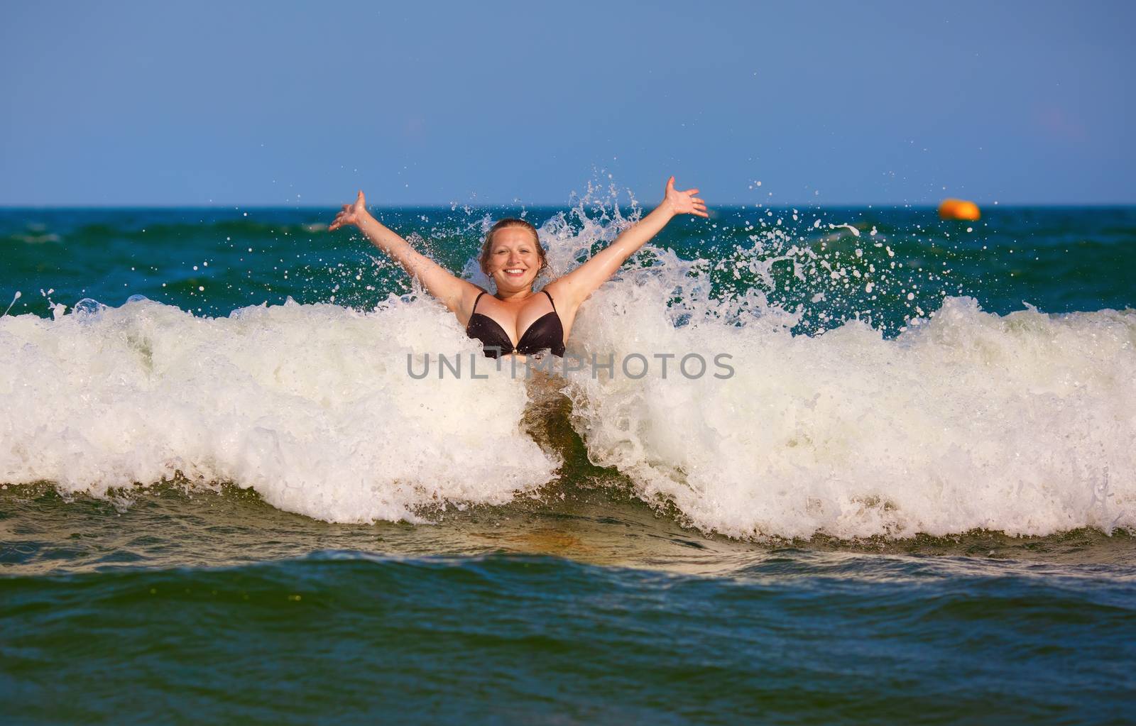 Beautiful smiling girl with her hands raised in the foam of a sea wave. Happy young woman. Bright sunny day.