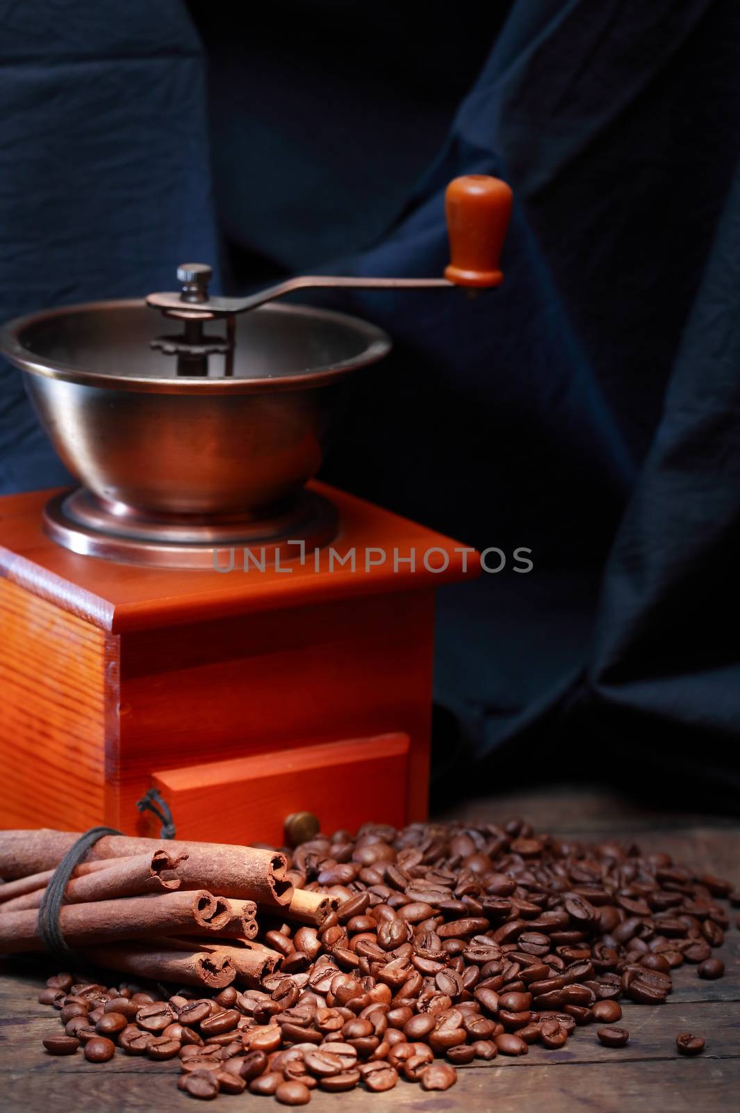 Coffee beans and cinnamon near vintage grinder on dark background