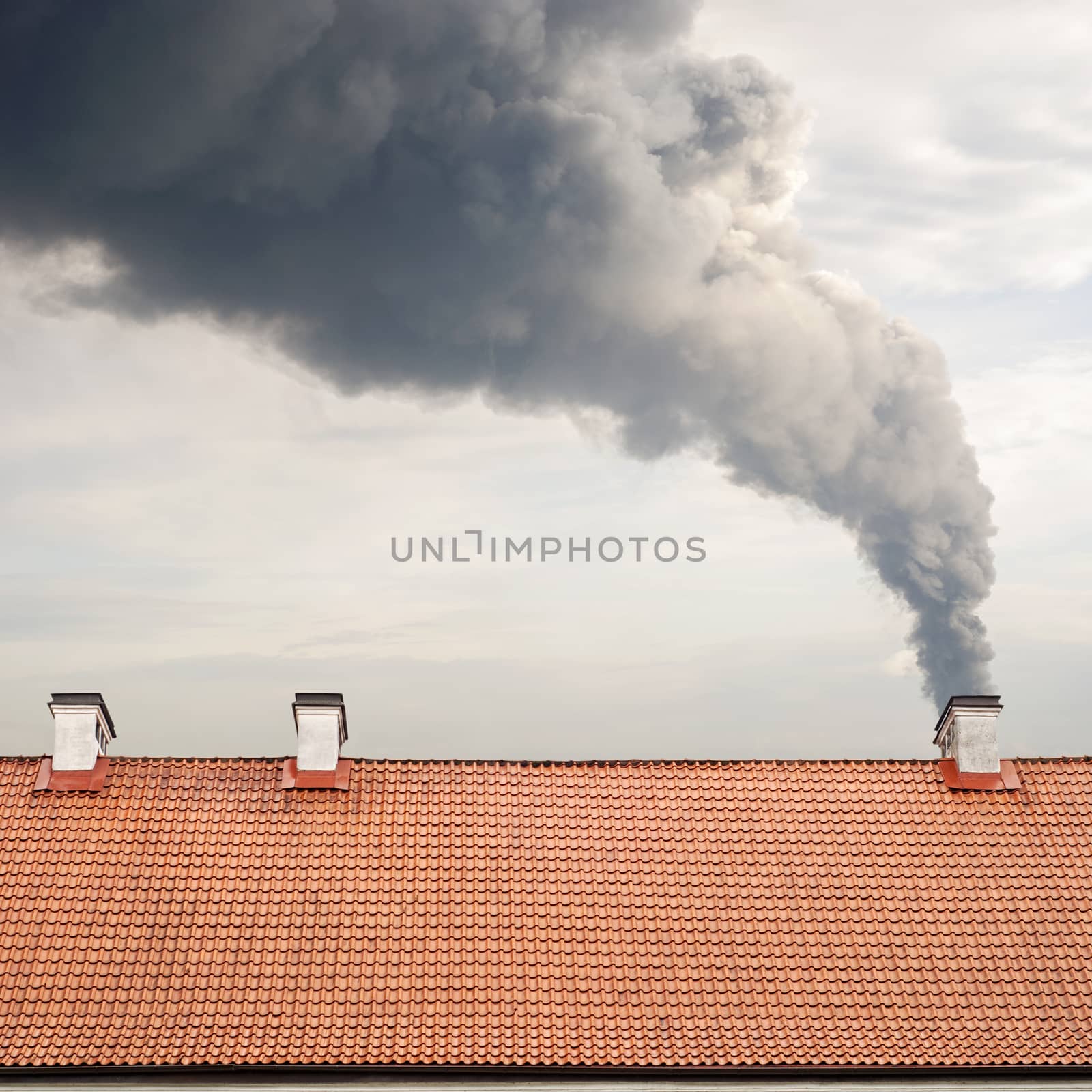 Huge dark smoke raising from a chimney, tiled brown roof 