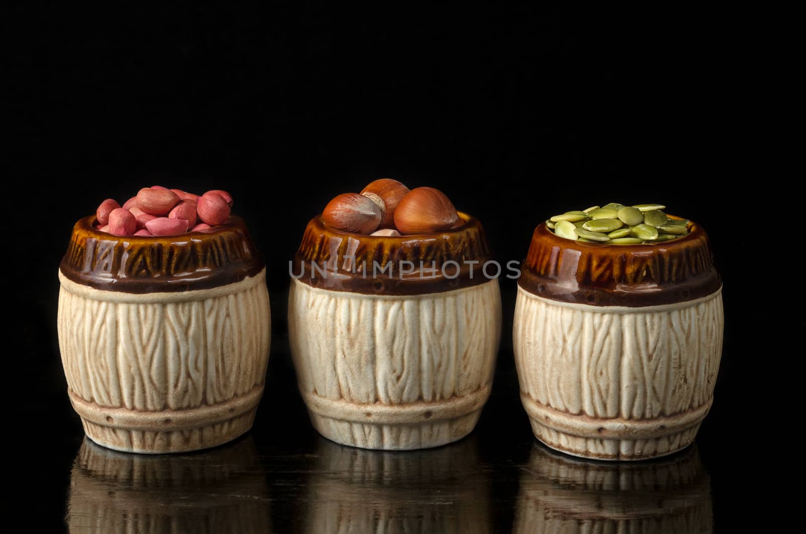 Nuts and seeds on black, antique lacquered surface and a black background. In a ceramic dish.