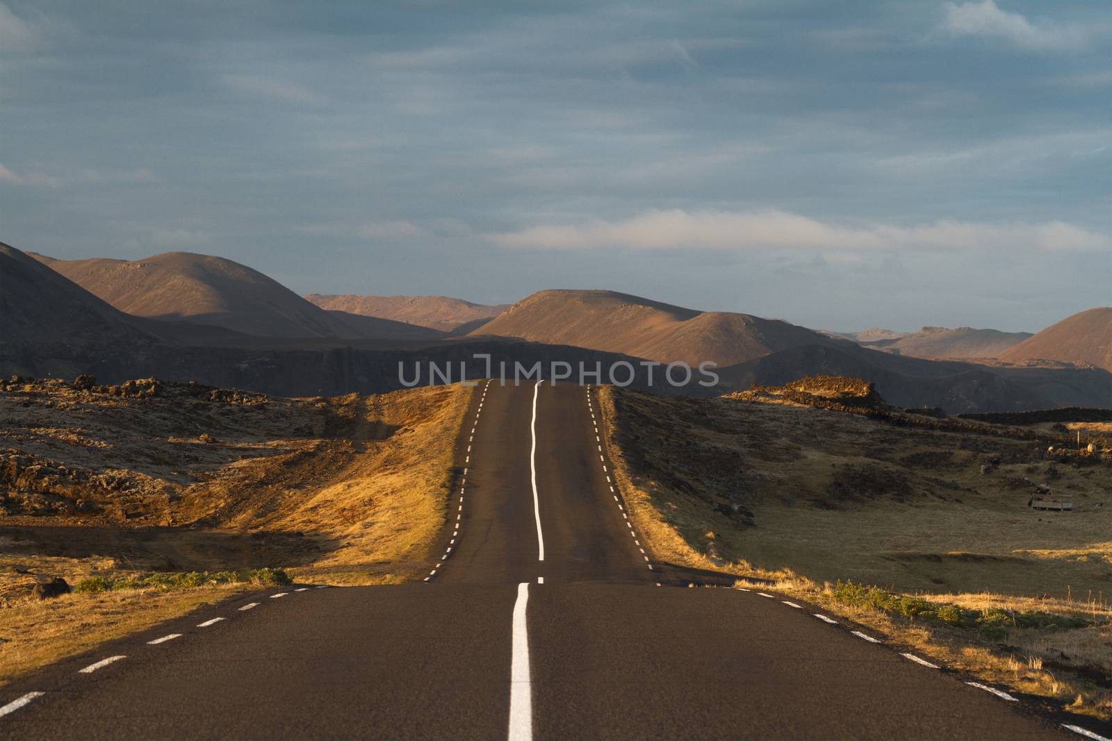 Horizontal photo at sunset of a straight asphalt road going into the mountains with clouds above in Reykjanes peninsula, Iceland