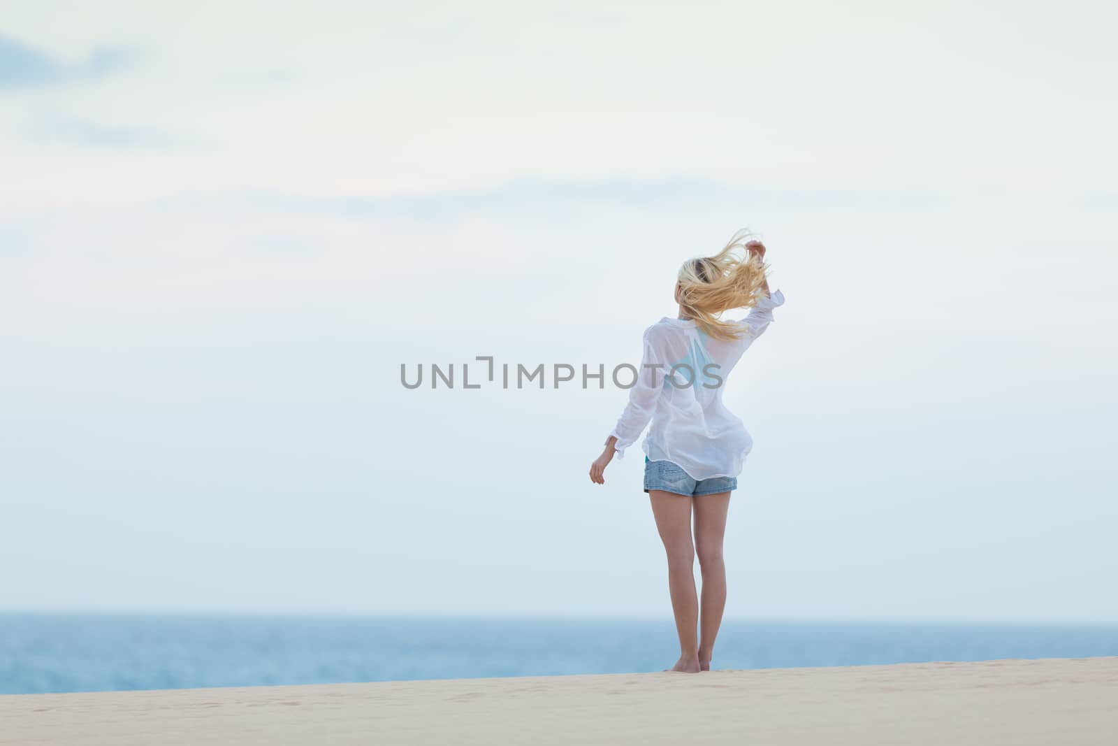 Meditative, sensual blonde woman wearing white loose casual shirt on vacations, looking at horizon, enjoying peaceful early morning.