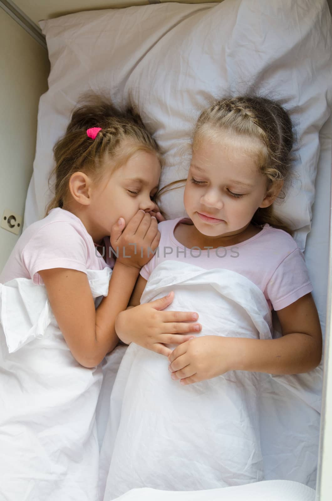 Two little girls sister sleep on a cot in a train
