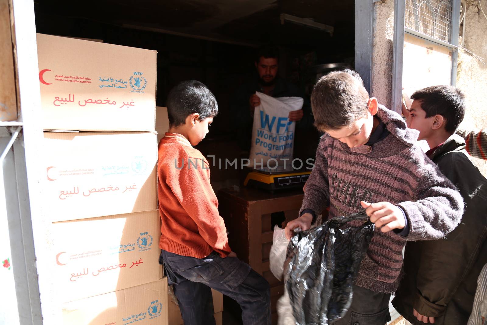 SYRIA, Saqba: A child carries a food pack as Syrian Red Crescent staff survey the delivery of humanitarian aid at a warehouse in Saqba, in the rebel-held Eastern Ghouta area, southern Syria, on the outskirts of the capital Damascus on March 15, 2016 during an operation in cooperation with the UN to deliver aid to thousands of besieged Syrians. UN aid convoys head to two Syrian towns besieged by government forces to deliver life-saving food and medicine to some 30,000 people, a UN spokesman said. 