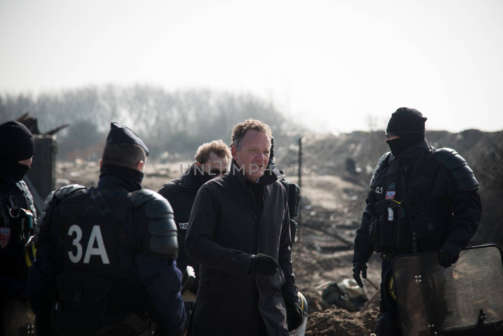 FRANCE, Calais: The deputy prefect of Pas de Calais, Vincent Berton walks past French anti-riot policemen standing guard during the dismantling of the southern part of the so-called 'Jungle' migrant camp in Calais, northern France, on March 14, 2016.Thousands of migrants have been living in the Jungle and other smaller camps along the northern coast, desperate to reach Britain where many have family or community ties and see better hopes of gaining employment or education. 