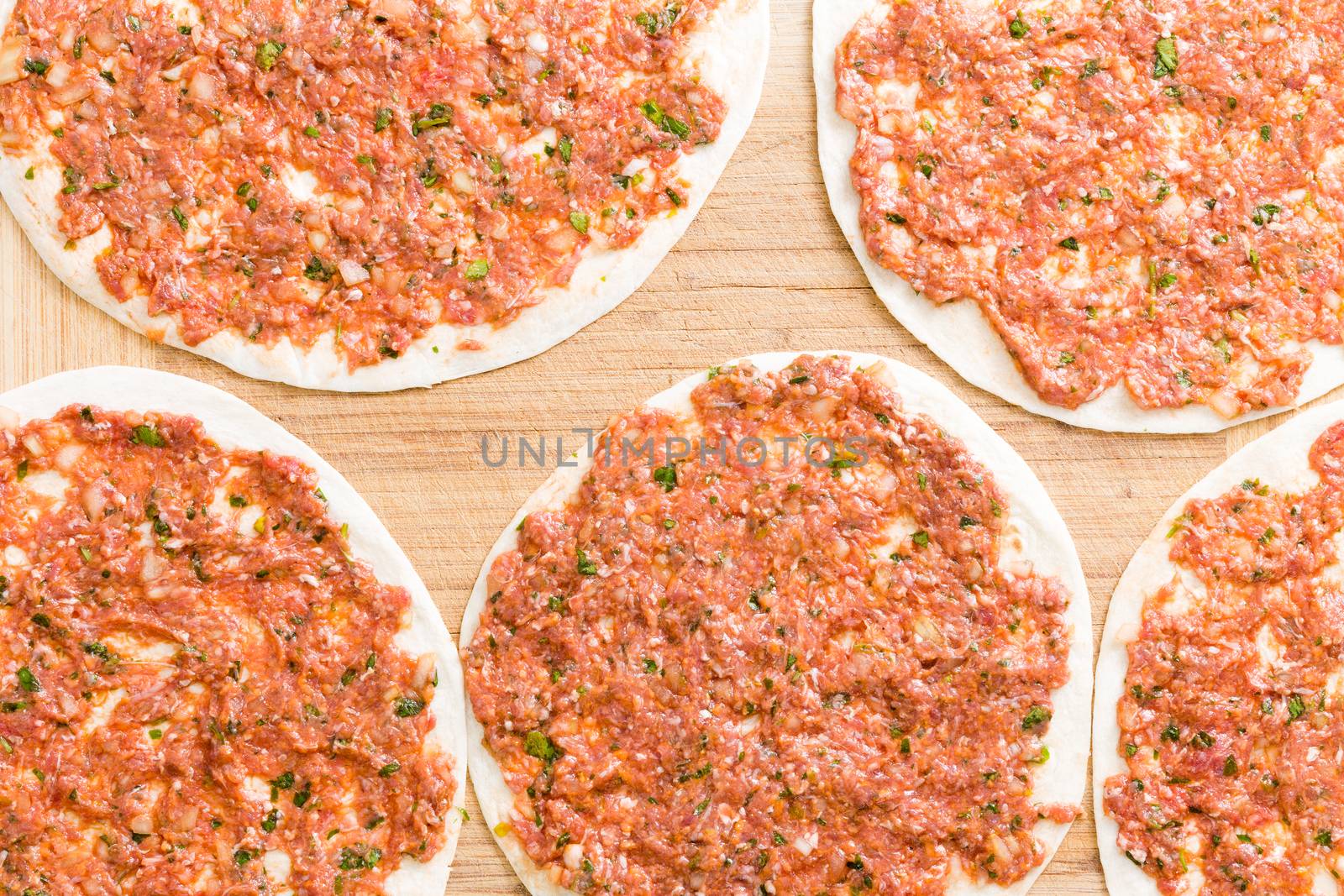 Homemade traditional Turkish lahmacun ready for the oven with round dough crusts topped with a tasty savory mixture of minced meat, vegetables and herbs, view from above