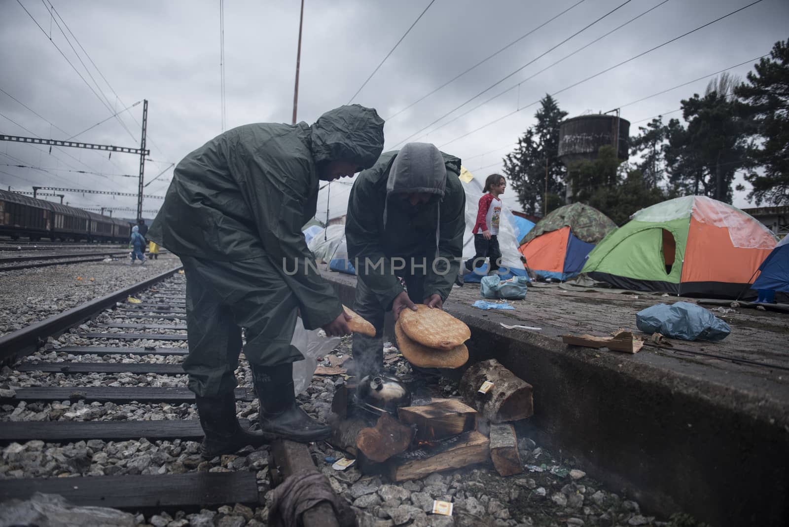 GREECE, Idomeni: Two men cook along the railway tracks next to tents at the Idomeni refugee camp on the Greek Macedonia border on March 15, 2016 in Idomeni, Greece. Yesterday, an attempt by some of the residents of the camp to cross the border to Macedonia was thwarted by Macedonian security forces who returned the migrants to Greece. The decision by Macedonia to close its border to migrants last week has left thousands of people stranded at the Greek transit camp. The closure, following the lead taken by neighbouring countries, has effectively sealed the so-called western Balkan route, the main migration route which has been used by hundreds of thousands of migrants to reach countries in western Europe, such as Germany. Humanitarian workers have described the conditions at the camp as desperate, which has been made much worse by recent spells of heavy rain.