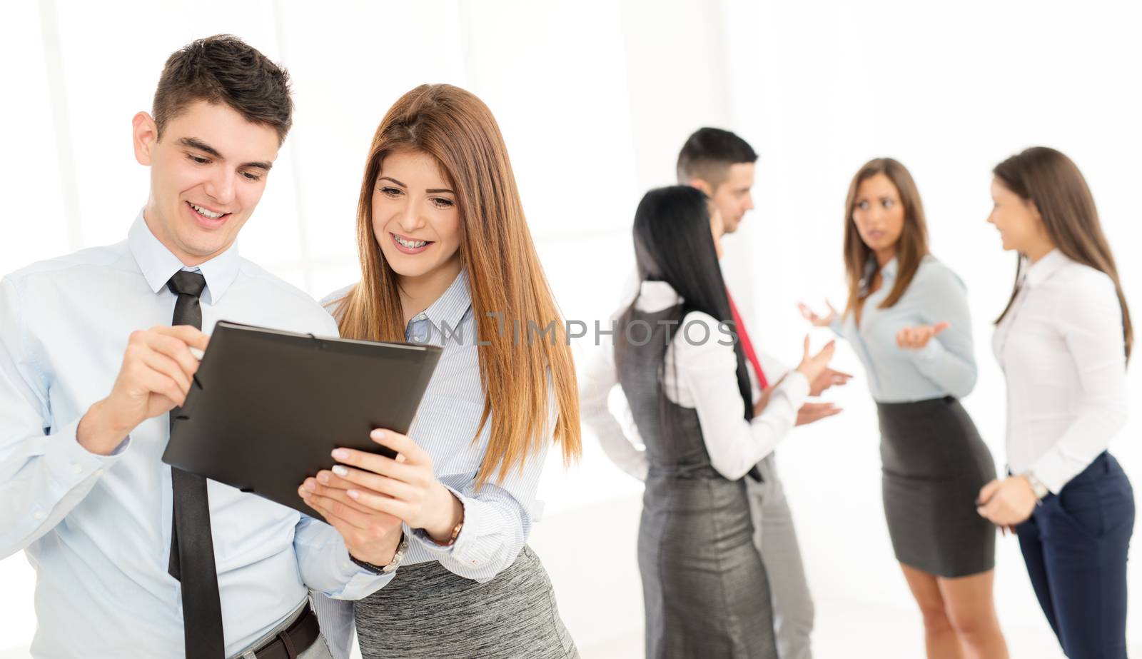 Two smiling young colleagues discussing in front their business team.