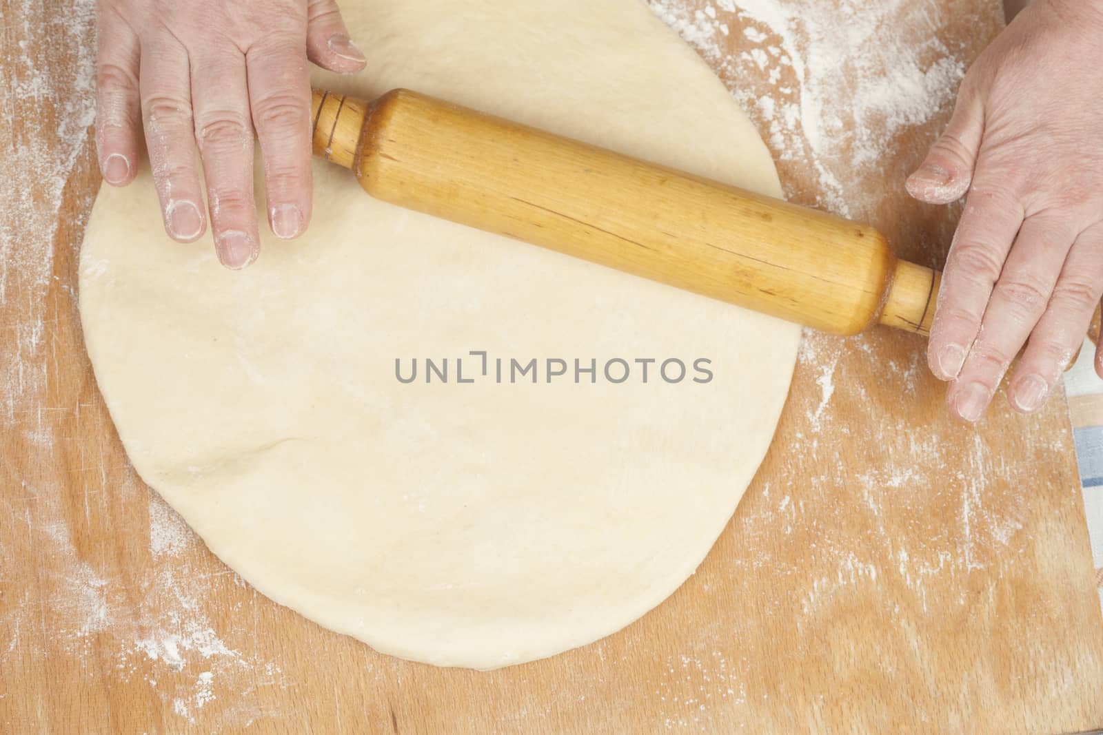 Hands baking dough with rolling pin on wooden table, depth of field