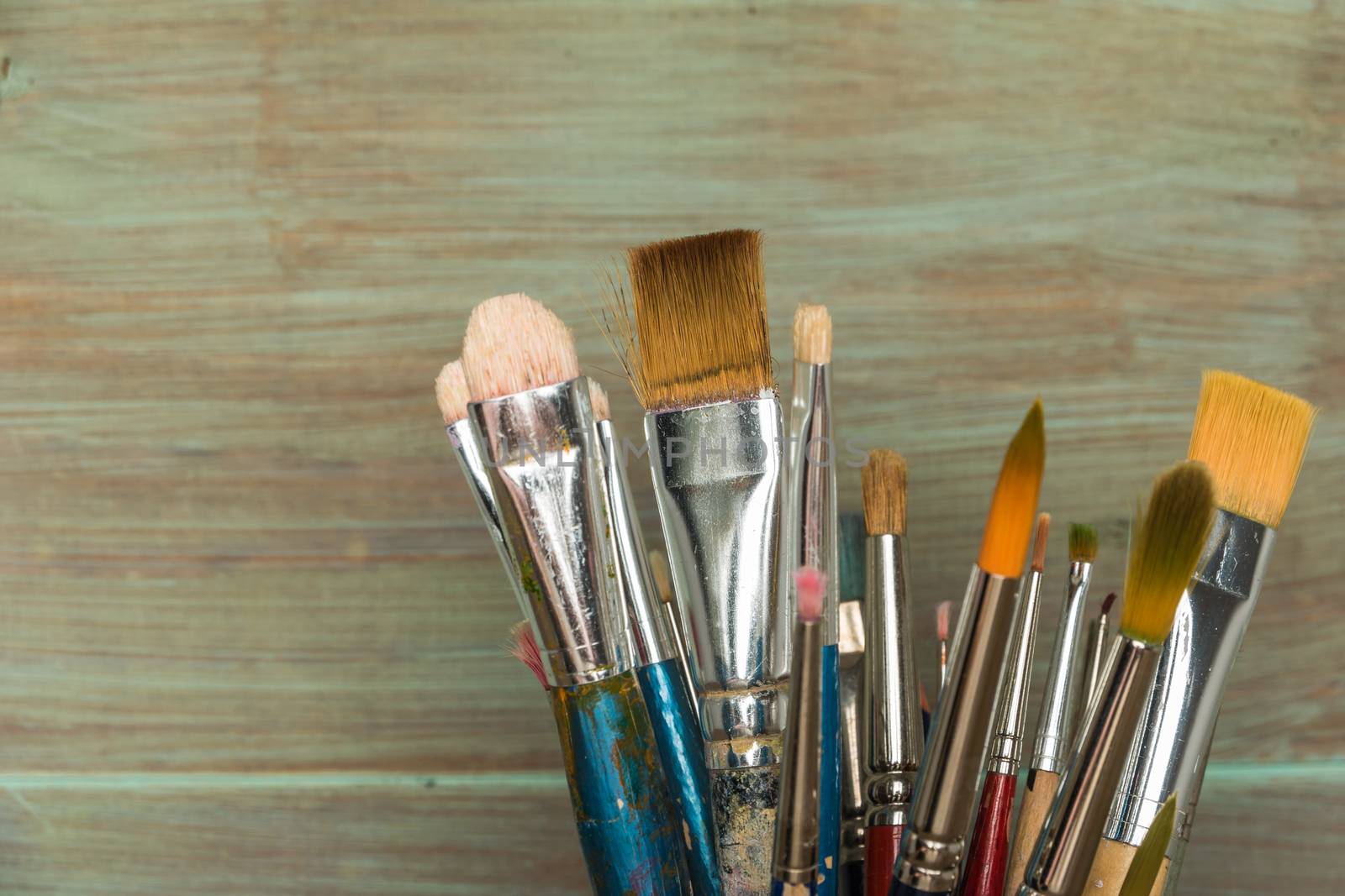 Artist paint brushes over rustic wooden texture. Top view with copy space.