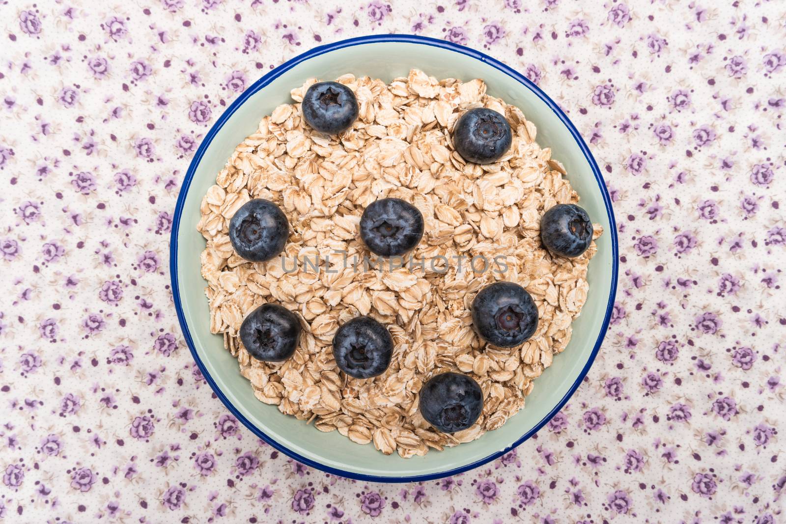 Oat flakes with blueberries in a bowl on cute fabric background. Top view with copy space.