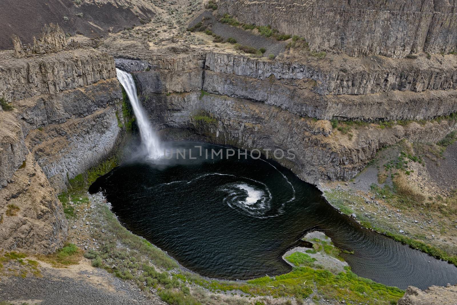 The canyon at the falls is 115 meters (377 feet) deep, exposing a large cross-section of the Columbia River Basalt Group. These falls and the canyon downstream are an important feature of the channeled scablands created by the great Missoula Floods that swept periodically across eastern Washington and across the Columbia River Plateau during the Pleistocene epoch. The ancestral Palouse river flowed through the currently dry Washtucna Coulee to the Columbia River. The Palouse Falls and surrounding canyons were created when the Missoula Floods overtopped the south valley wall of the ancestral Palouse River, diverting it to the current course to the Snake River by erosion of a new channel. The area is characterized by interconnected and hanging flood-created coulees, cataracts, plunge pools, kolk created potholes, rock benches, buttes and pinnacles typical of scablands. Palouse Falls State Park is located at the falls, protecting this part of the uniquely scenic area.
