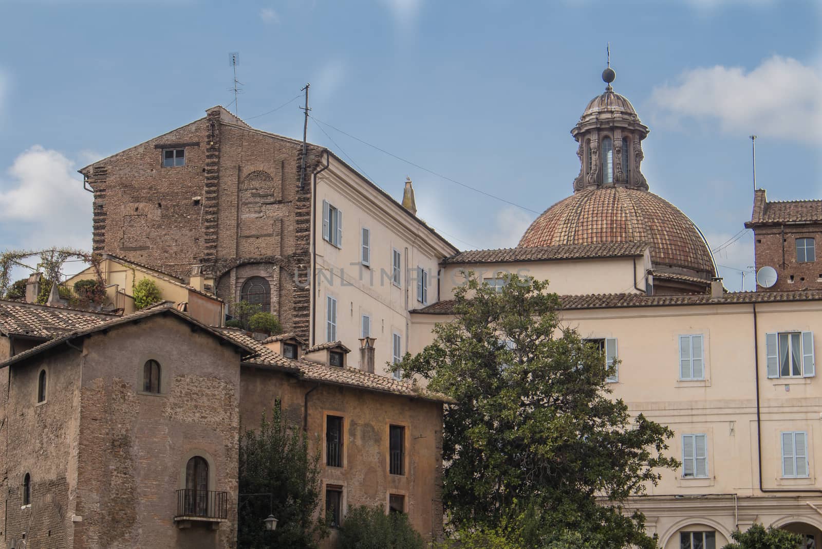 All shades of orange color of the facades of the roman houses. Dome of a church in the background. Blue sky with white clouds.