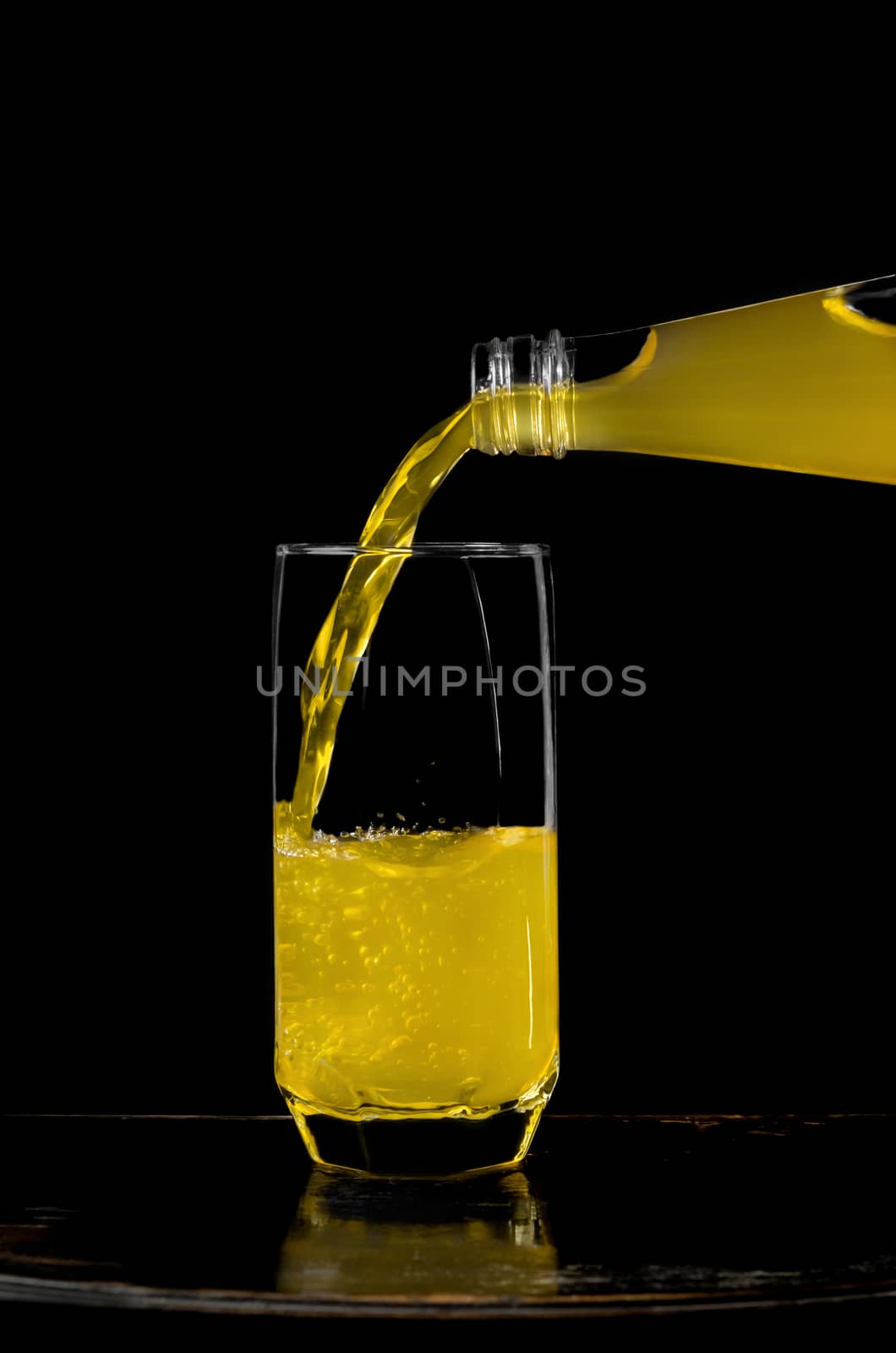 Lemonade pouring from bottle into a half full glass. Black background.