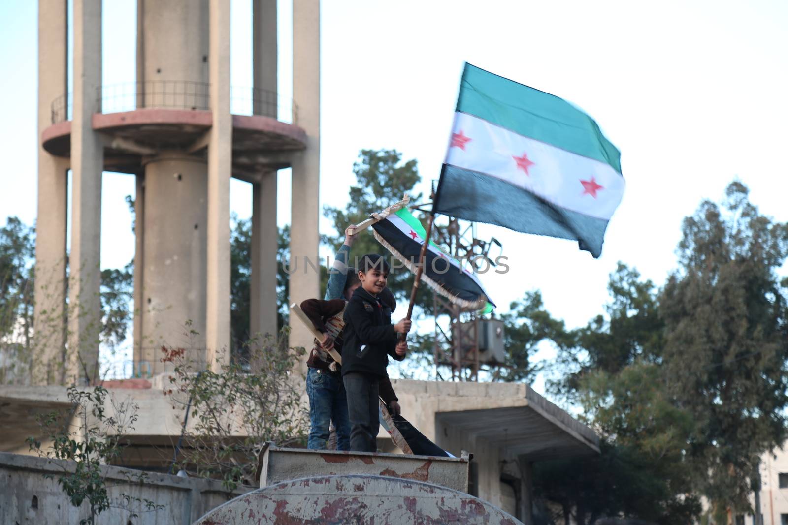 SYRIA, Saqba: Children hold a pre-Baath Syrian flag, that was adopted by the Syrian revolution during the uprising, on March 16, 2016 in Saqba, near Damascus, southern Syria, during a protest to mark the fifth anniversary of Syria's revolution. The conflict began with anti-regime protests in mid-March 2011 and spiralled into a bloody war after a harsh government crackdown on demonstrators. 