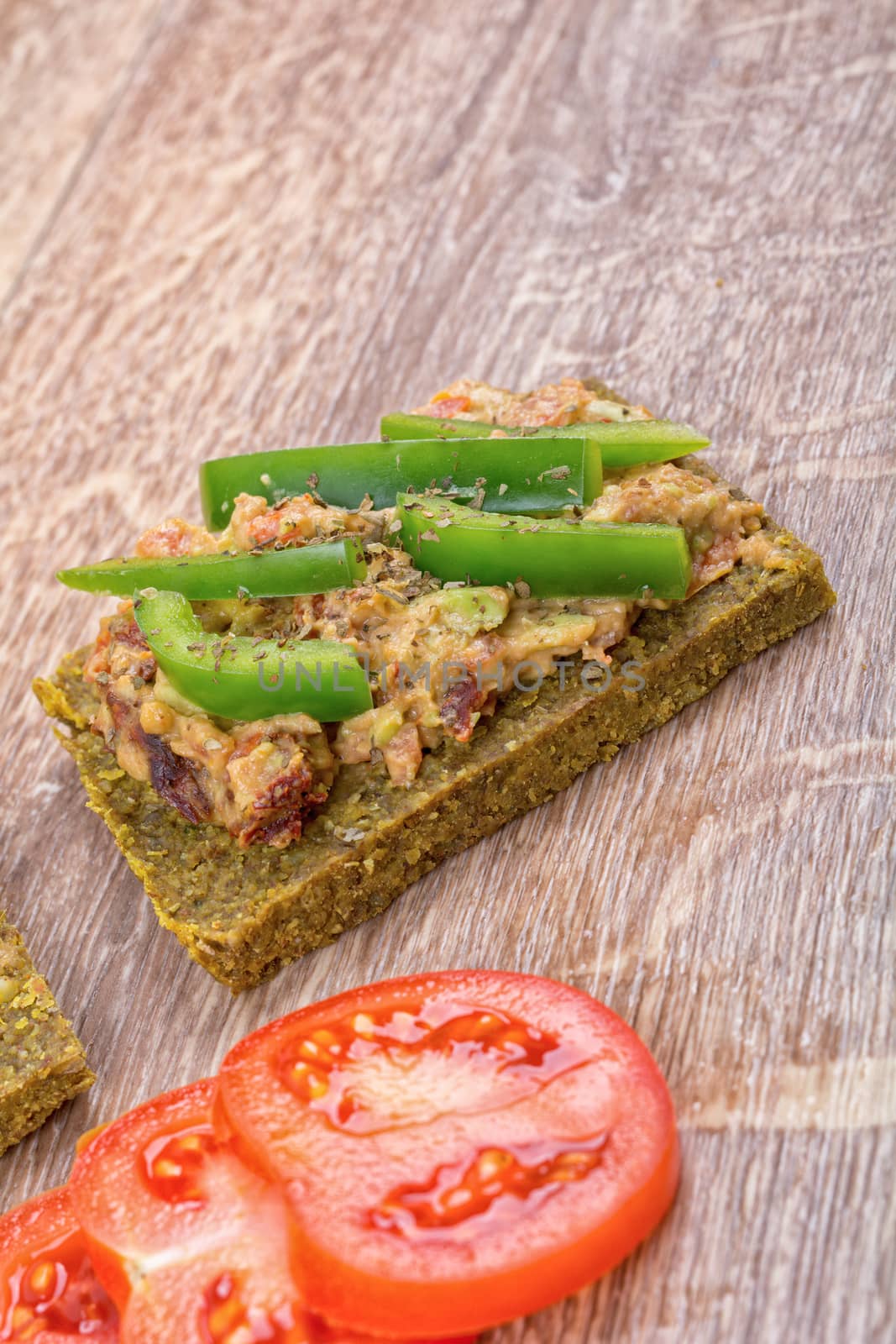 Raw bread with a spread decorated with green pepper and tomatoes