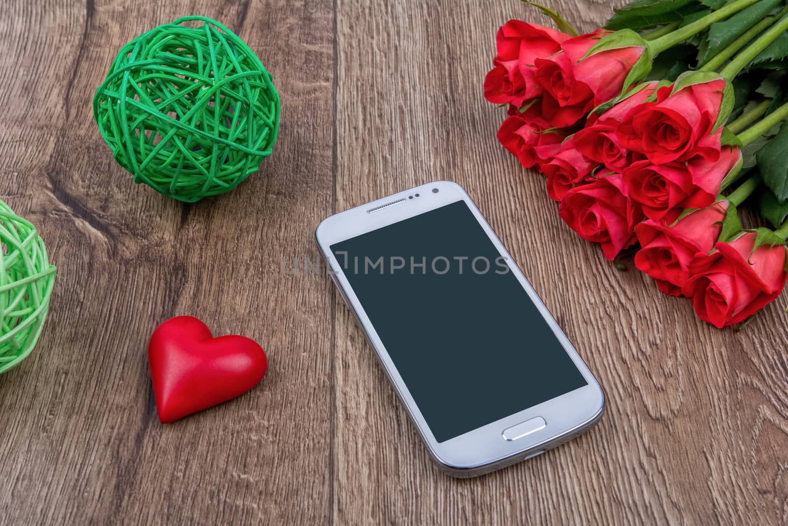 Mobile phone, red heart and red roses on a wooden background