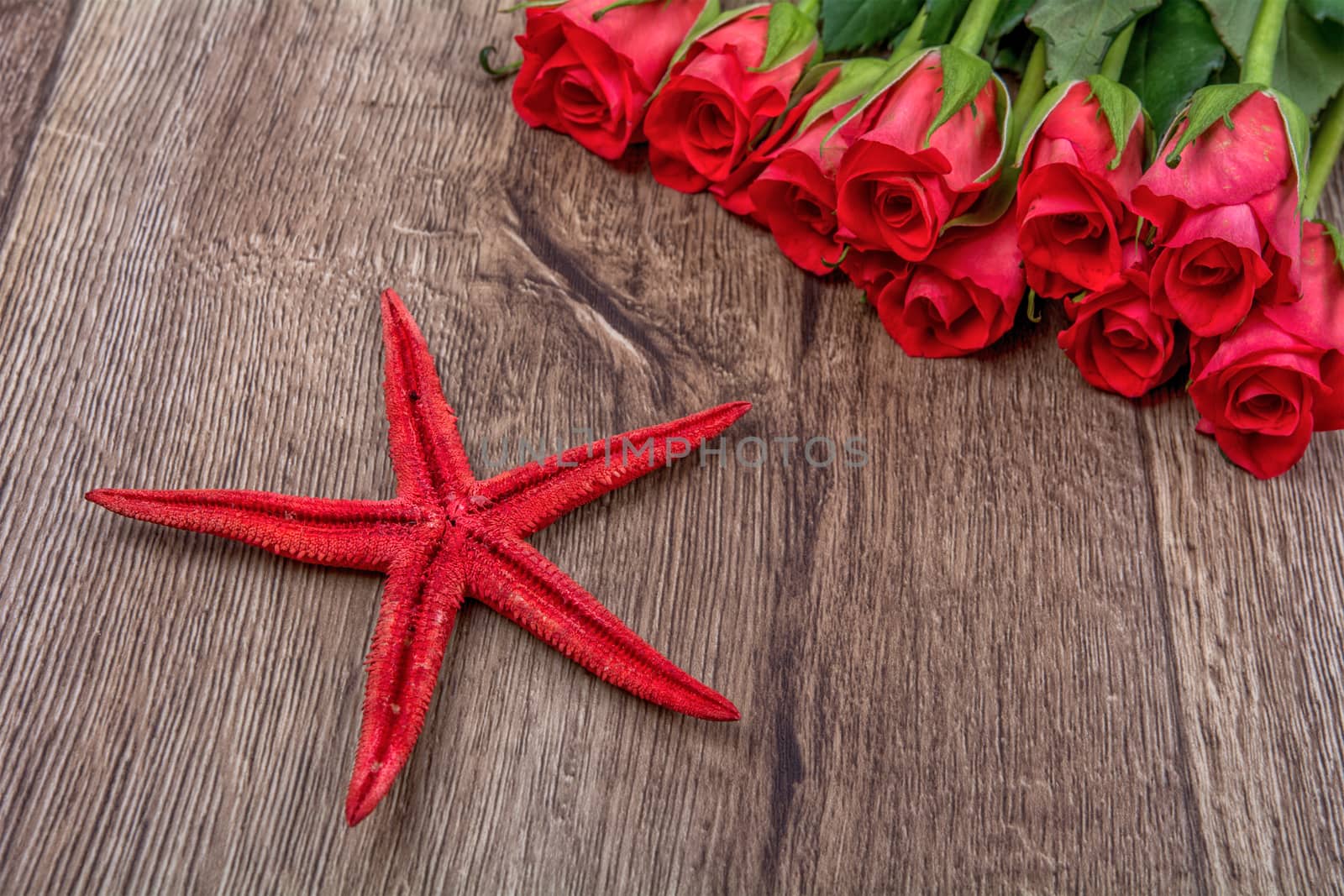 Red starfish and red roses on a wooden background