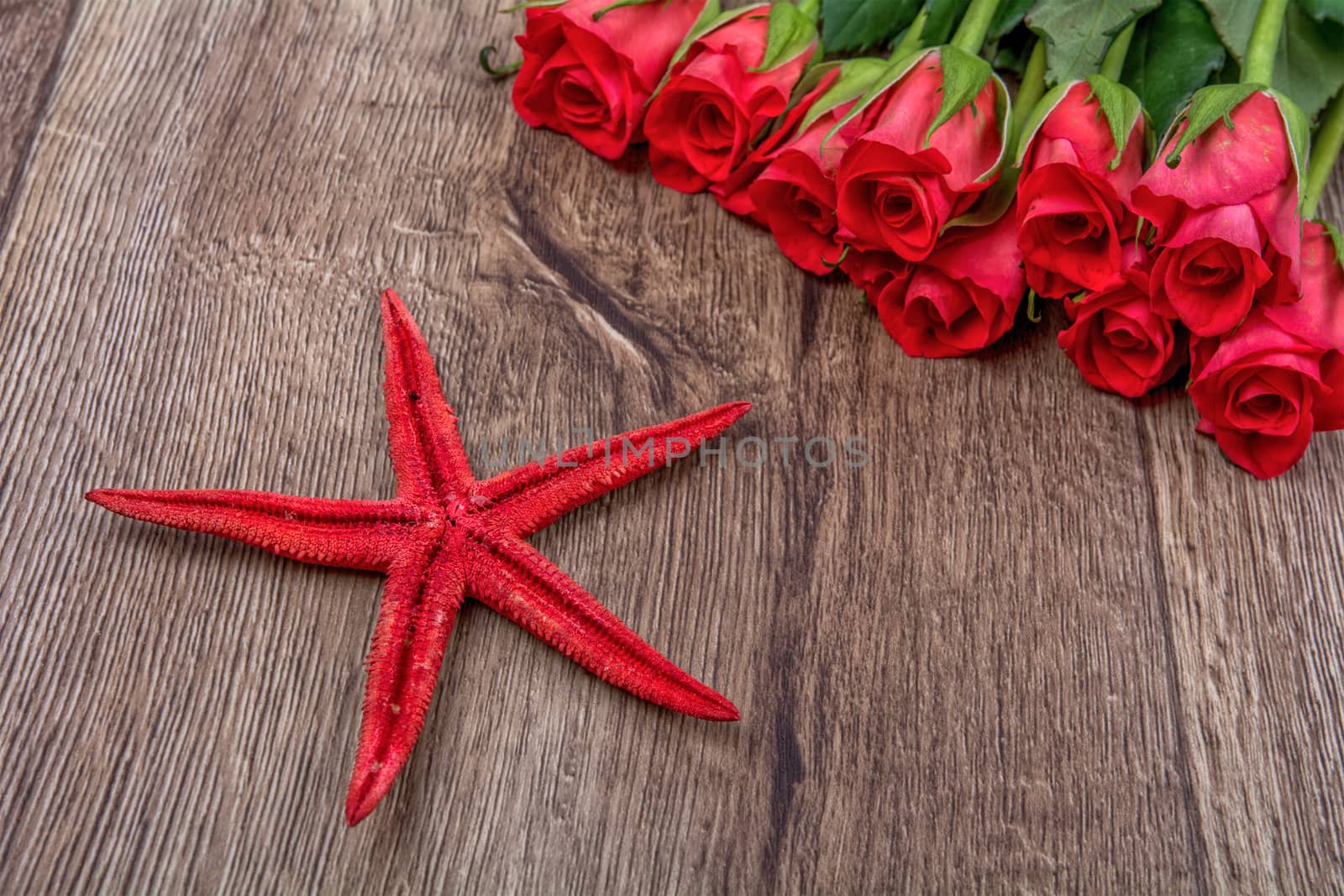 Red starfish and red roses on a wooden background