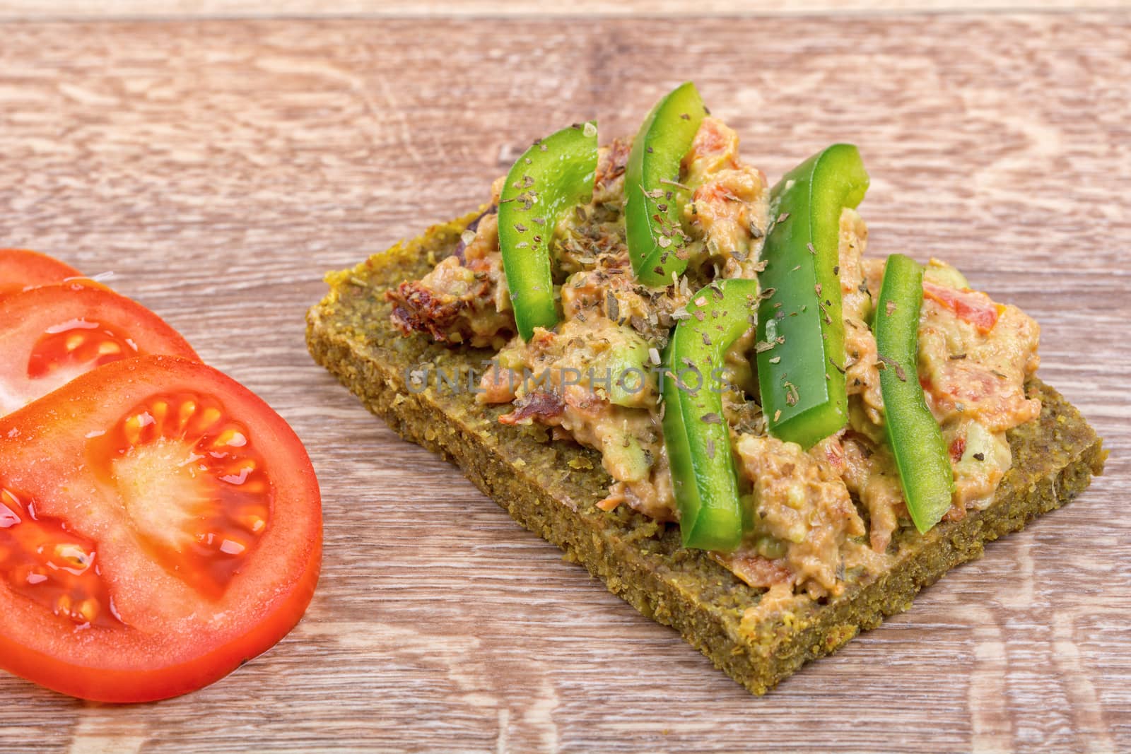 Raw bread with a spread decorated with green pepper and tomatoes