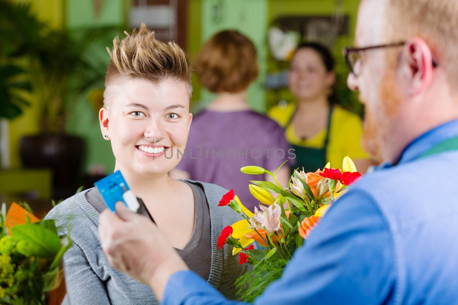 Cute female customer in a busy flower shop using credit card