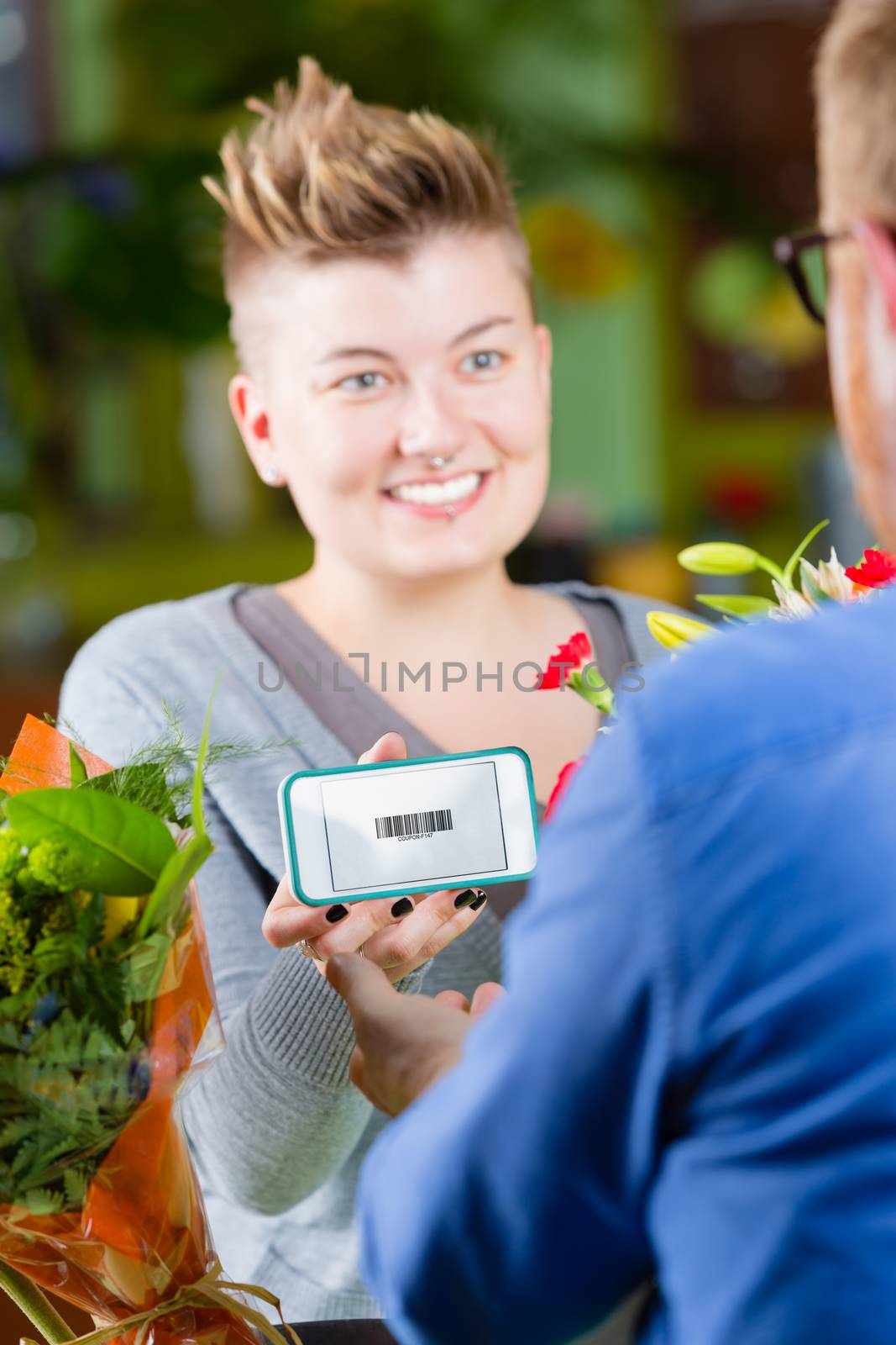 Young female customer in a busy flower shop using electronic coupon
