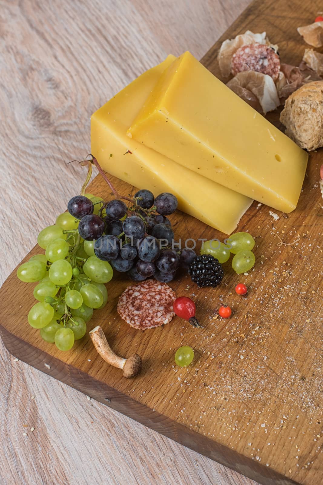 Fresh grapes, cheese bacon berries and salami on wooden table