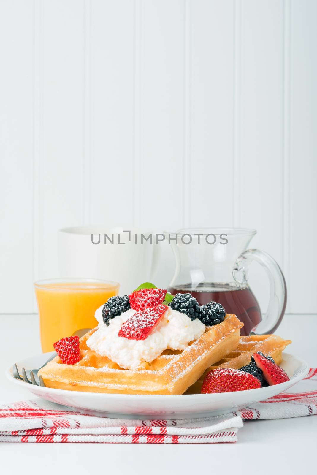 Plate of fresh waffles with berries, coffee and orange juice.