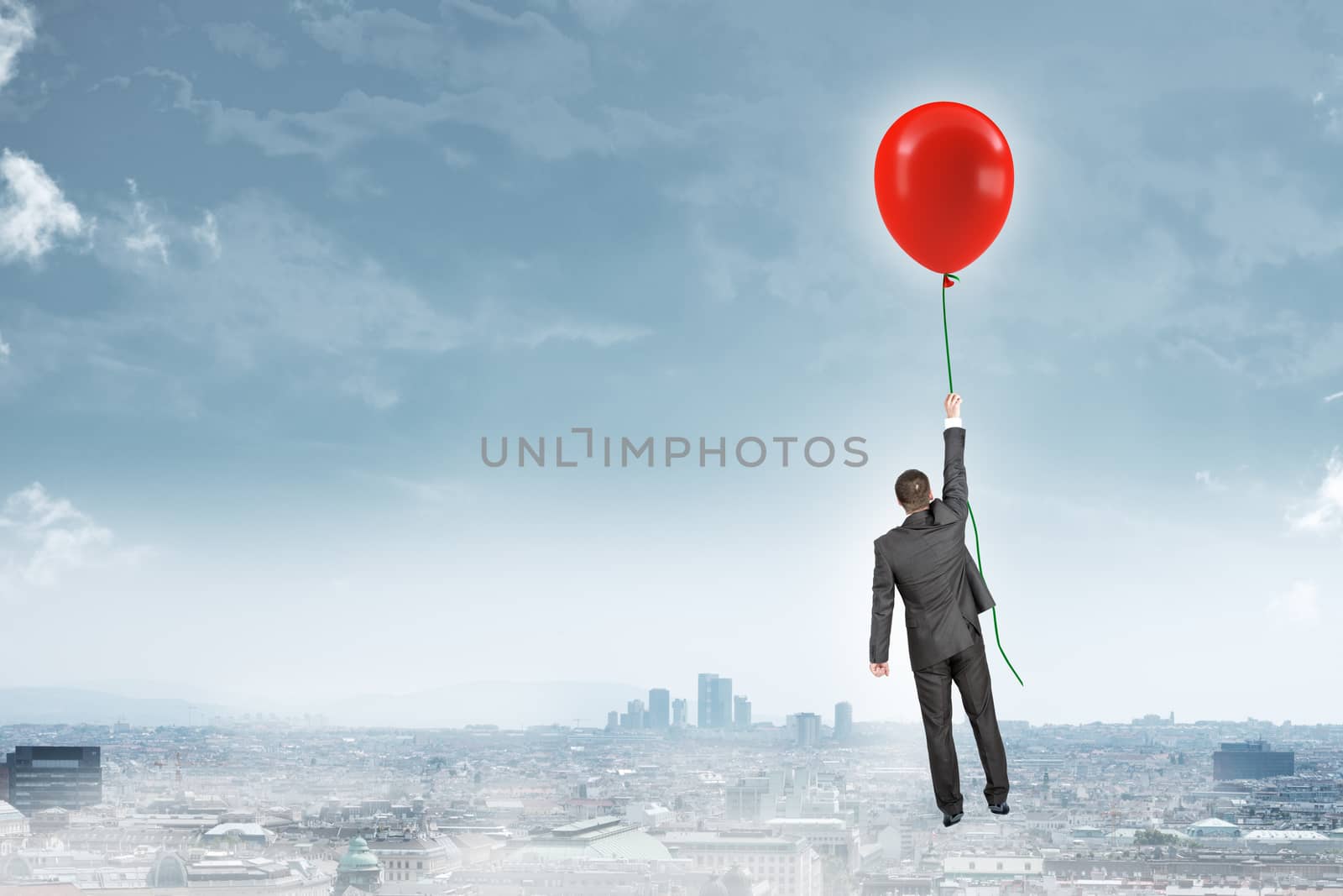 Businessman holding balloon and flying above city, rear view. Business concept