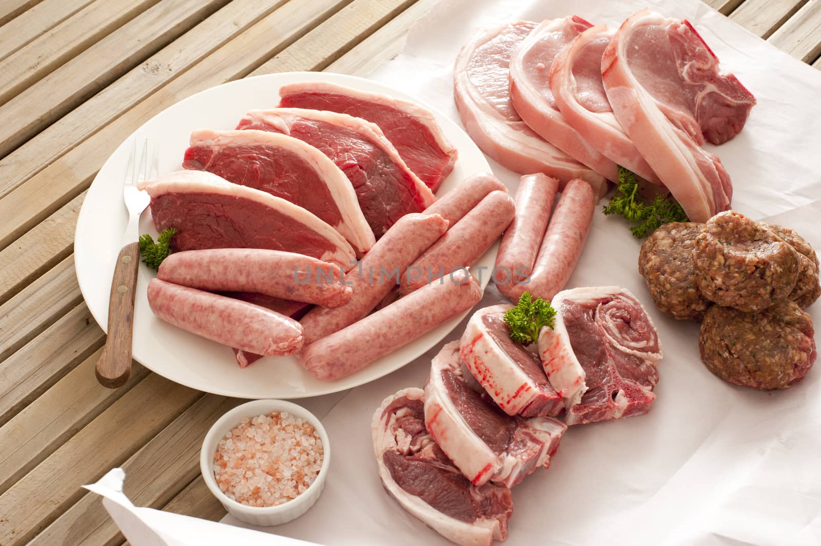 Large assortment of raw meat on a table with sausages, pork, lamp chops patties and beef steaks ready for a summer BBQ
