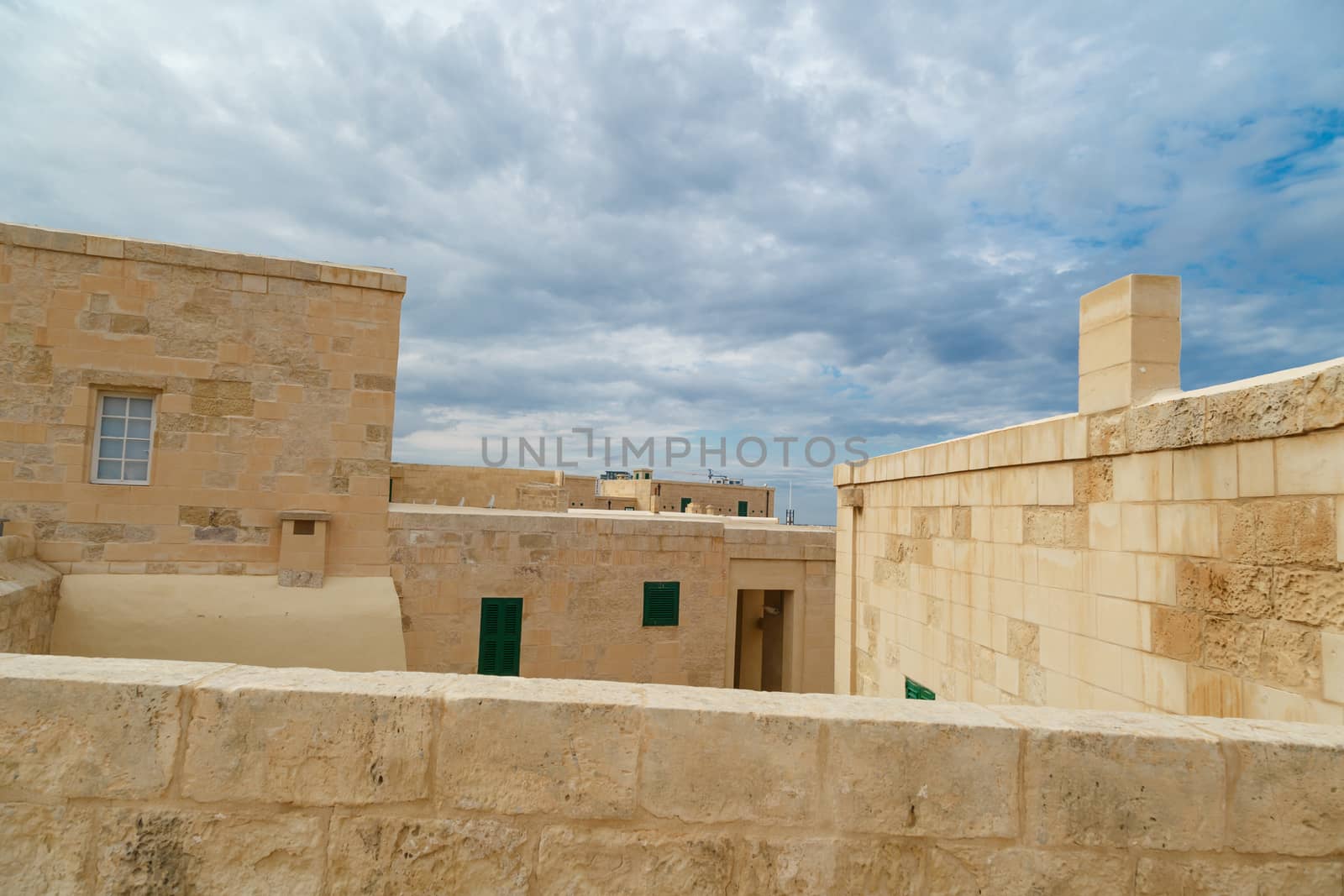 View of National War Museum in Valletta, Malta with high yellow stone walls, on cloudy sky background.
