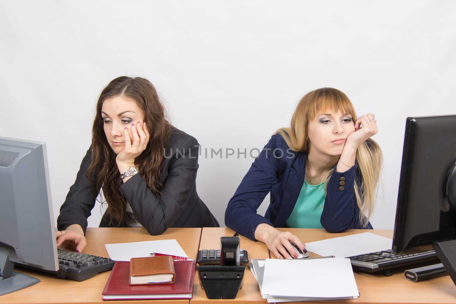 Two young office employee wearily sitting behind a desk
