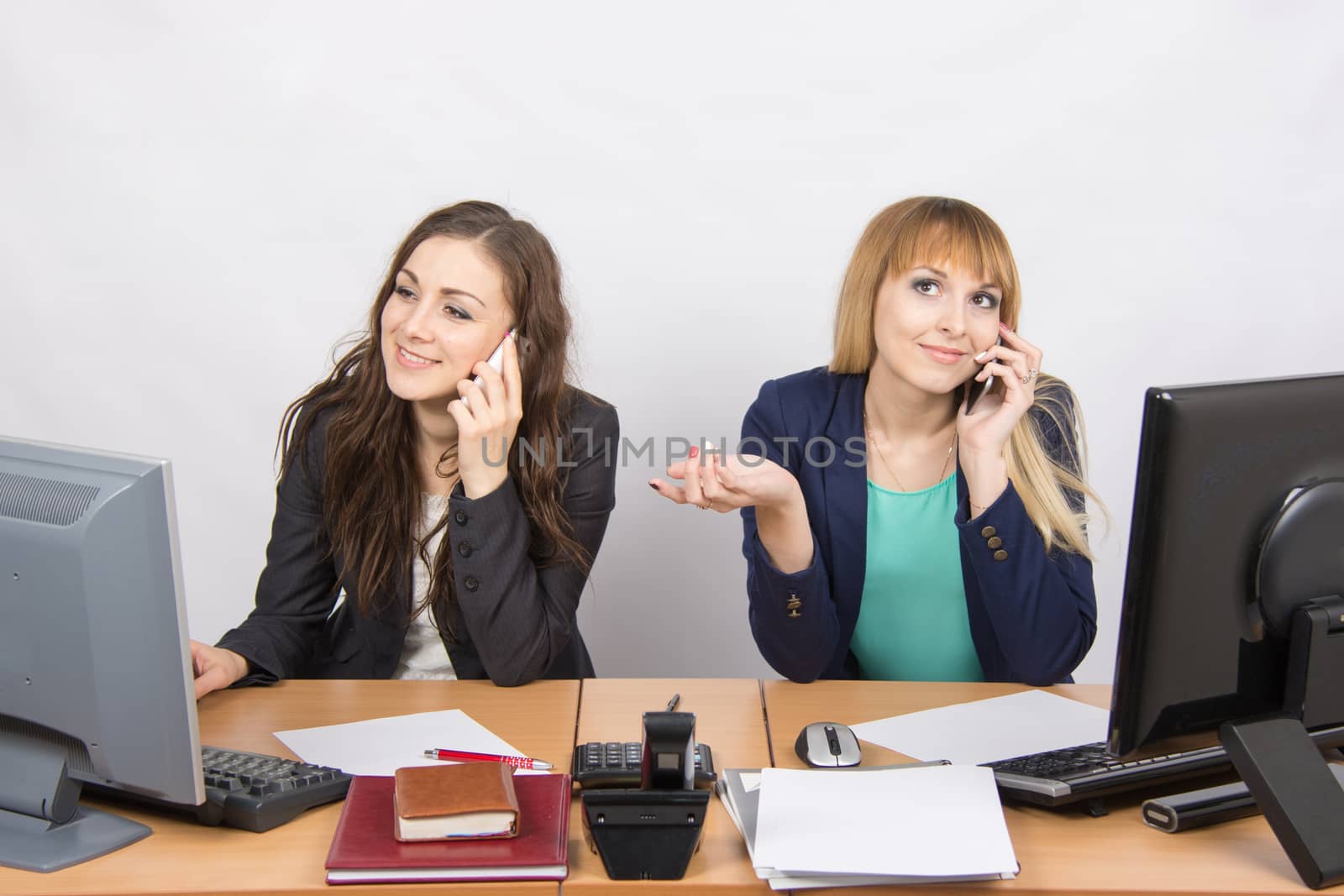 Two girls at a desk talking on mobile phone in the office by Madhourse