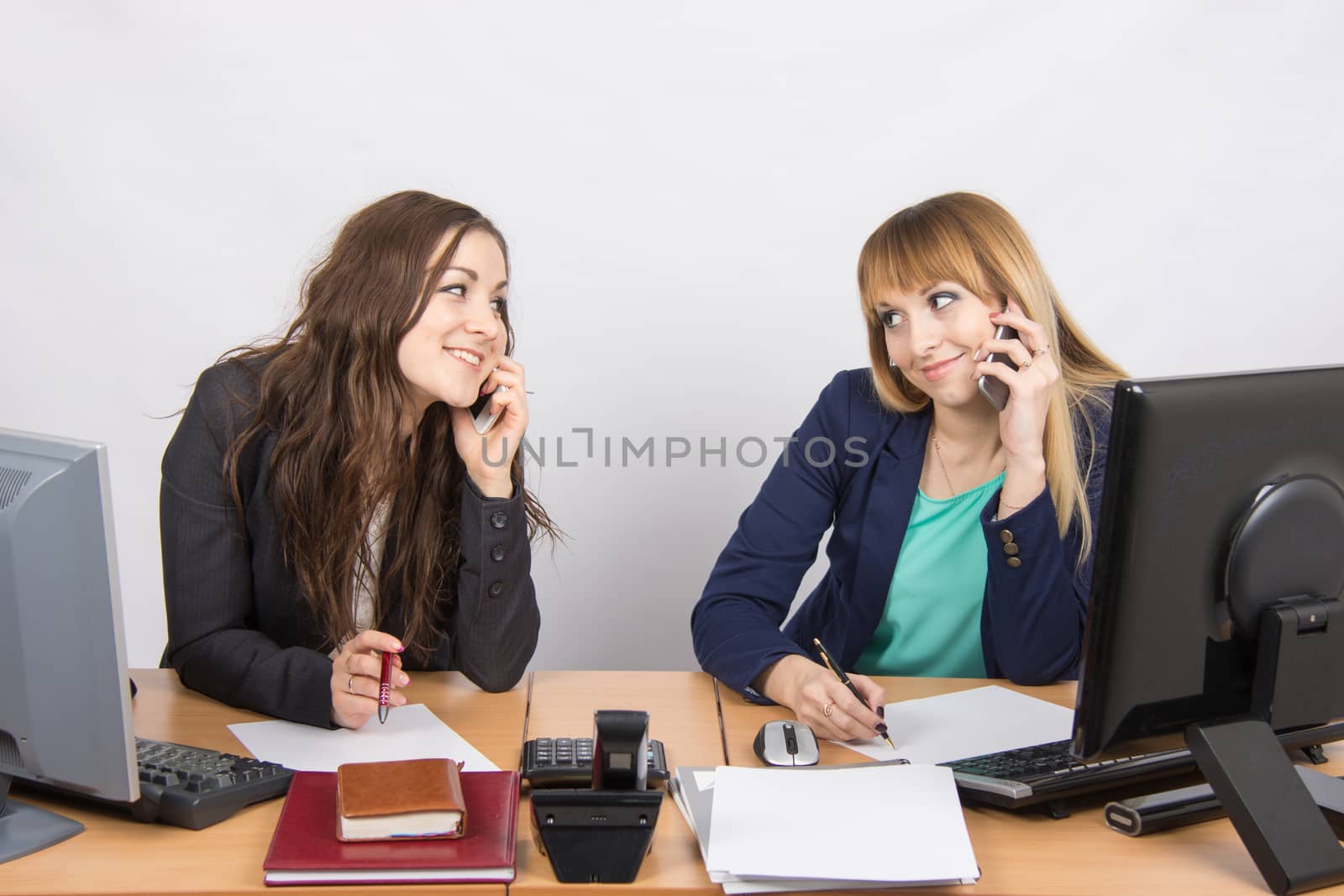 Two young office employee talking on mobile phones at his desk