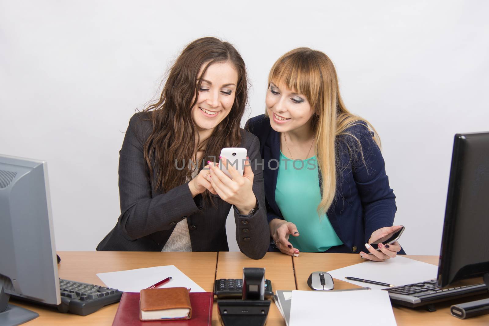 Two young office employee engaged in private affairs in a mobile phone at his desk