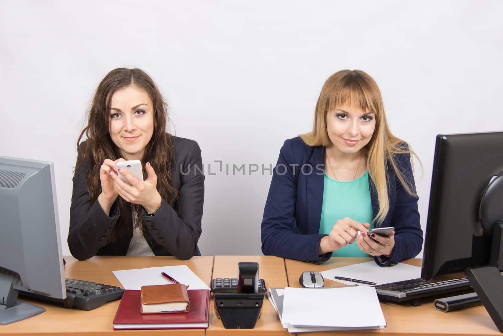 Two young office employee engaged in personal business in mobile phones at his desk
