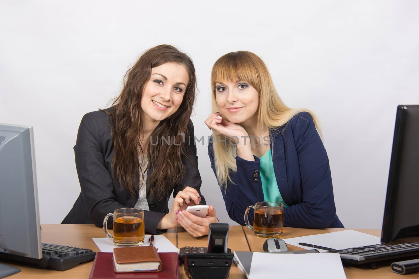 Two young beautiful girls office talking over a cup of tea