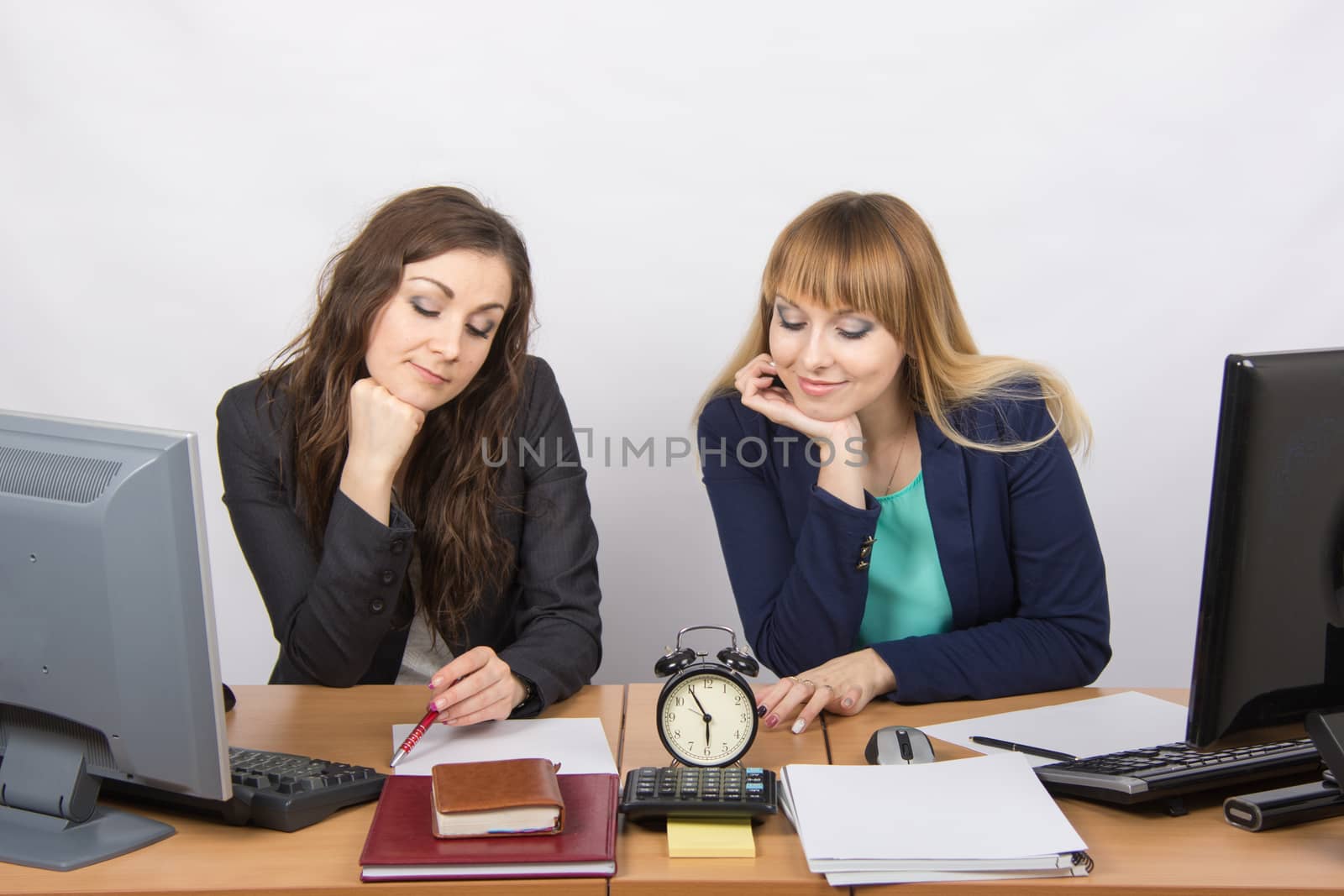 Two bored office worker waiting for the end of the day and look at the clock