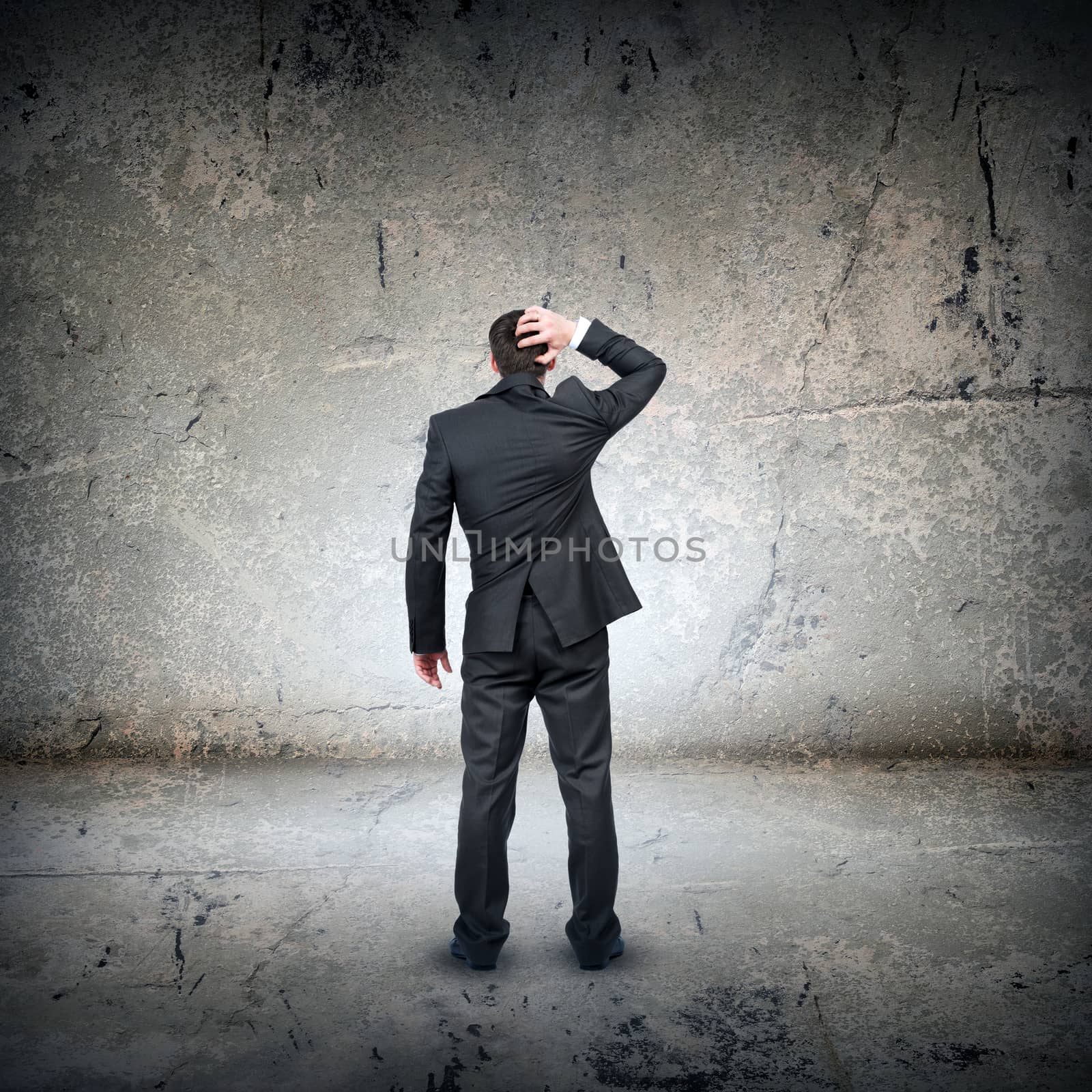 Confused businessman in front of grey wall, rear view