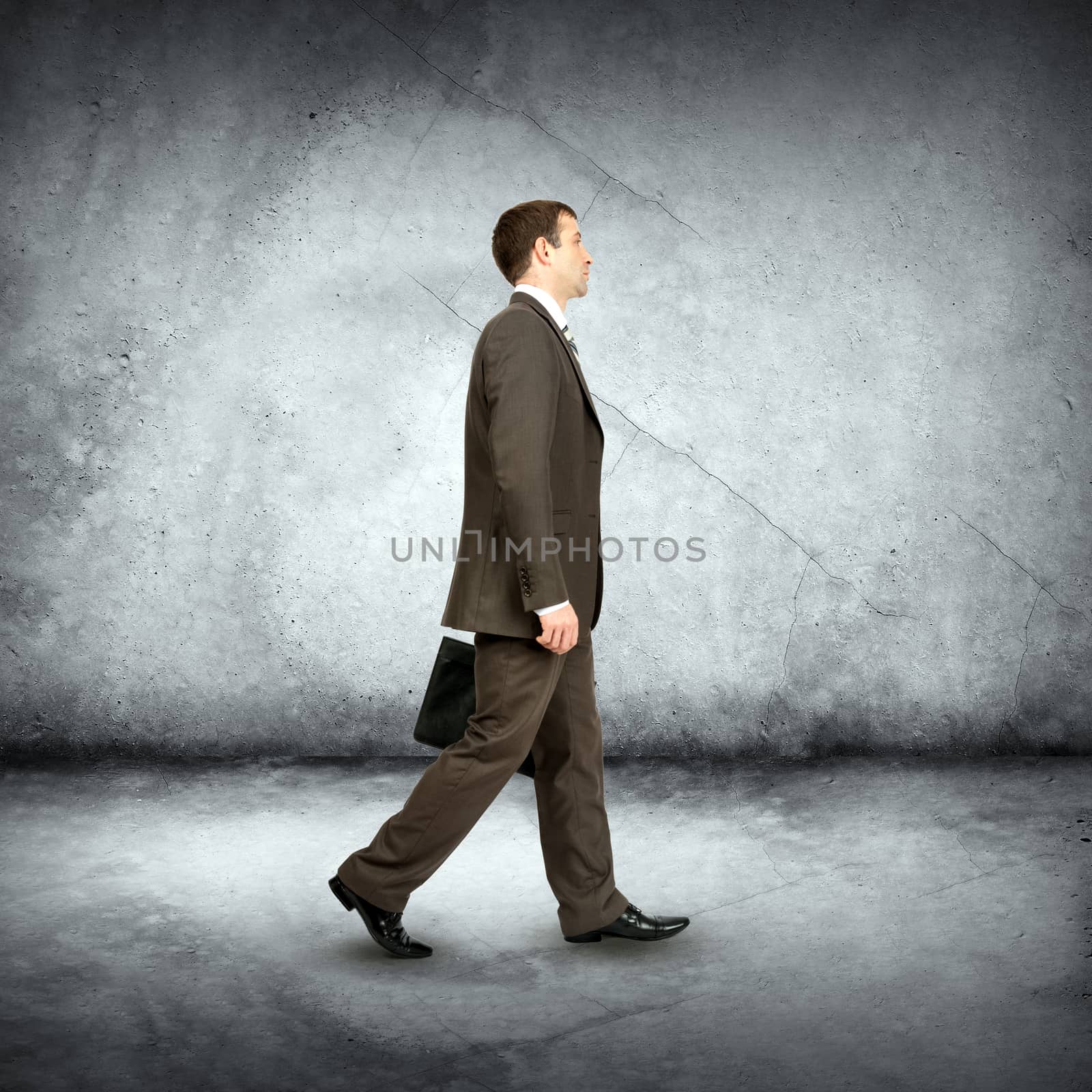 Businessman with suitcase walking on grey wall background
