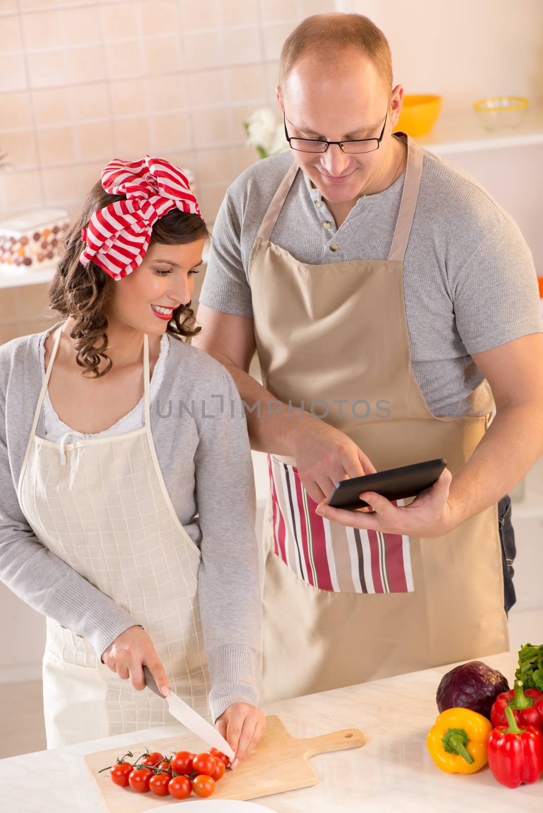 Happy couple reading recipe for tablet and preparing food in the kitchen