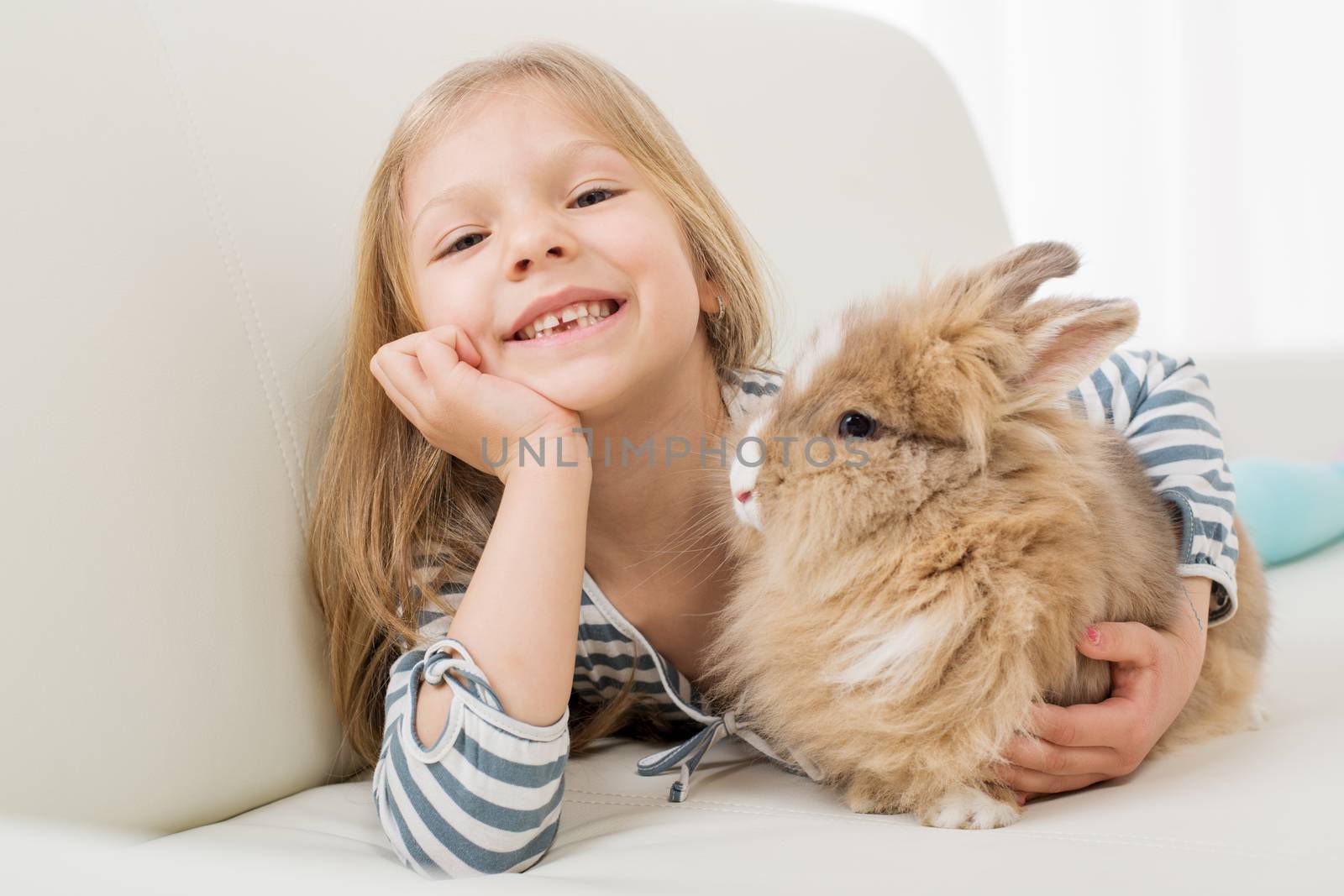 Little girl with her bunny laying on the sofa and hugging